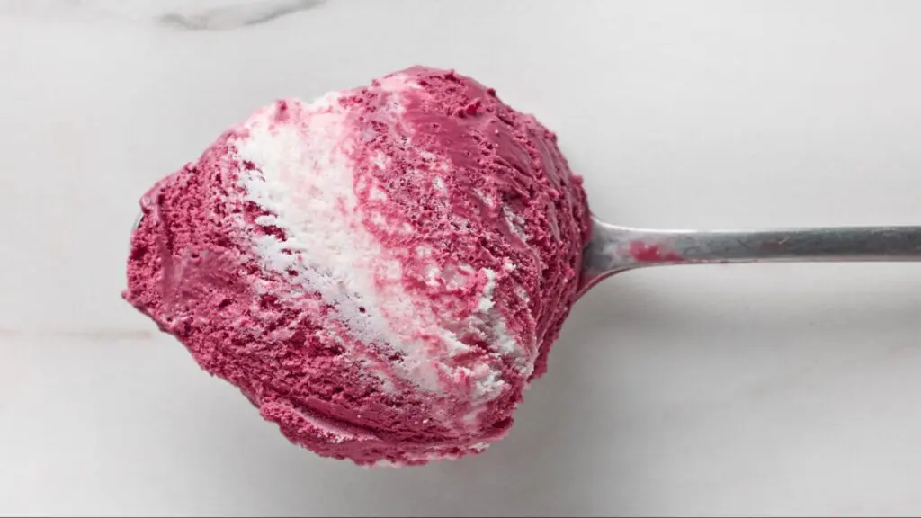 Close-up of a metal spoon holding a scoop of swirled raspberry and vanilla ice cream against a white background