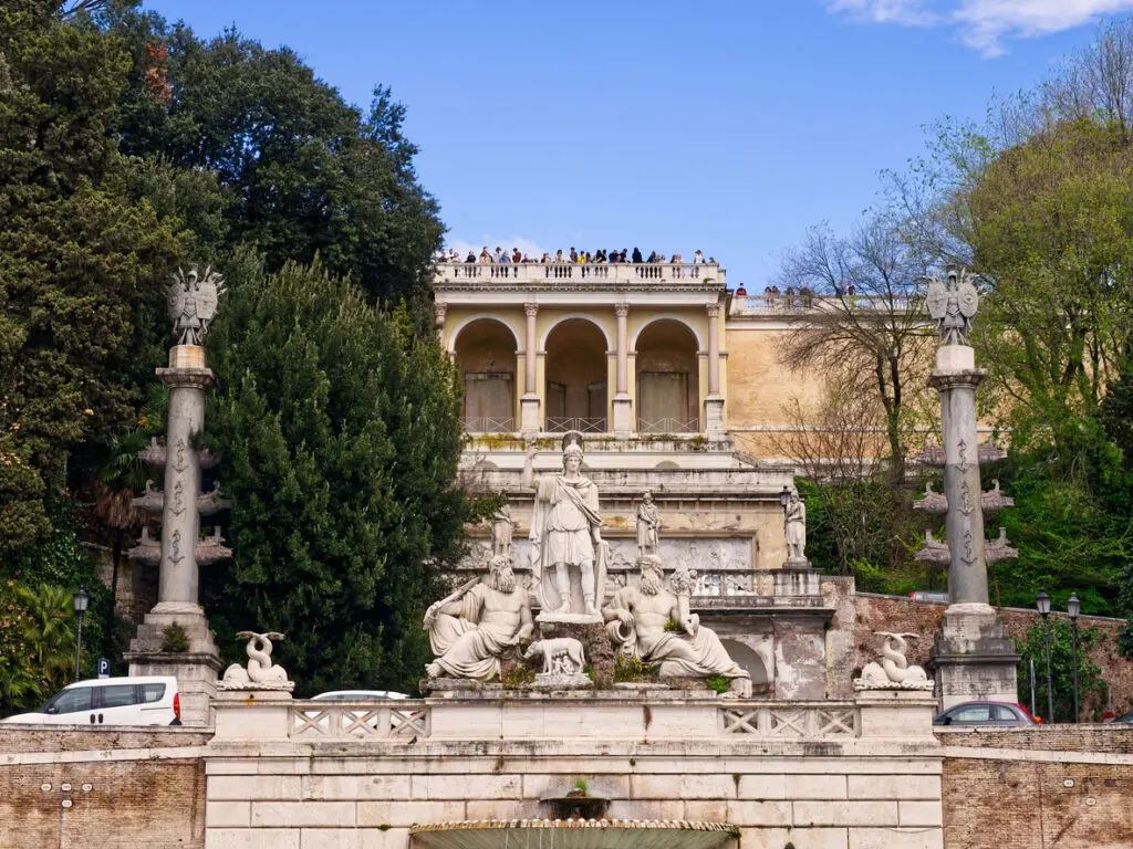View of the Fountain of the Goddess Roma and terrace at the Pincian Hill entrance to Piazza del Popolo in Rome, Italy, with classical sculptures and tourists above