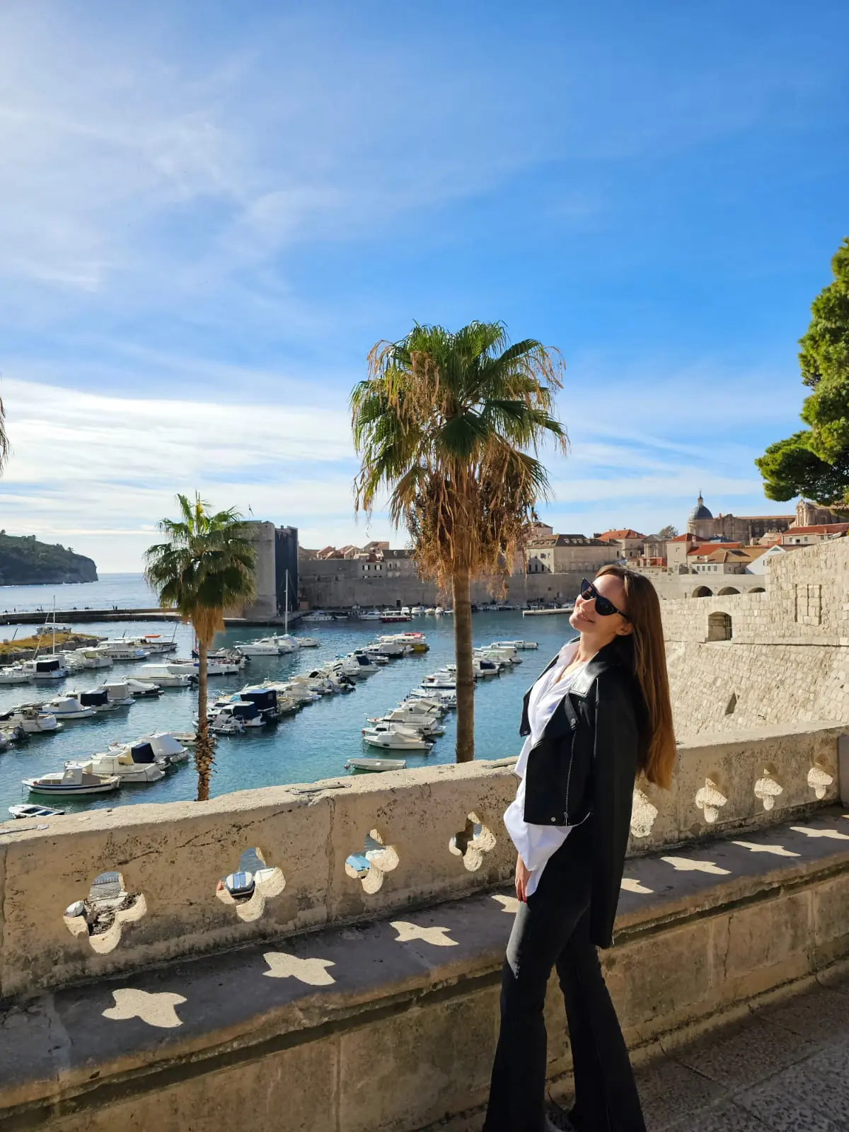 A young woman smiling to the camera with a fortified seaside town in the background.