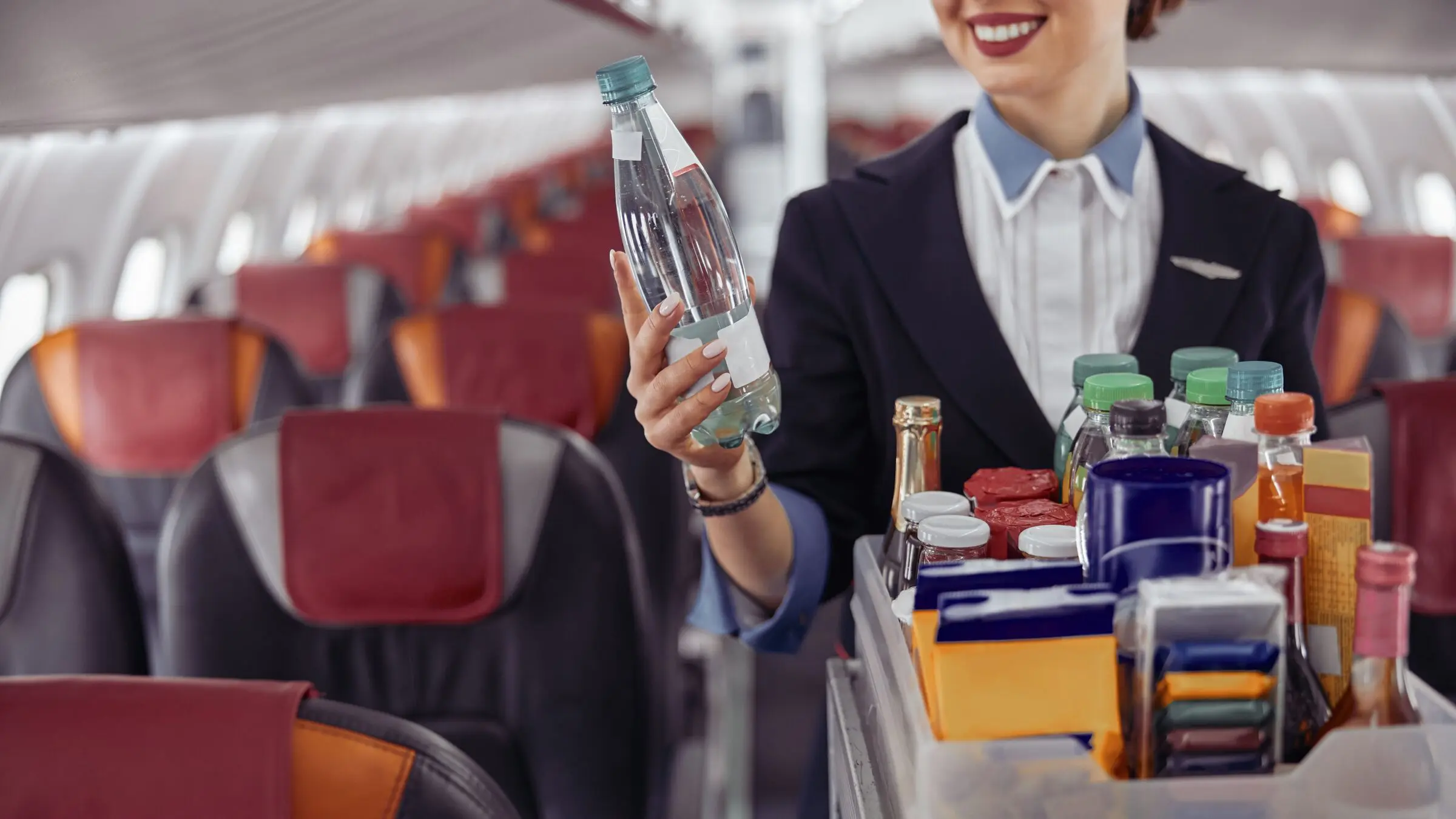 A flight attendant is holding a water bottle in the passenger cabin of an airplane jet.