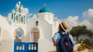 A woman with her back turned to the camera is admiring a whitewashed church in Santorini.