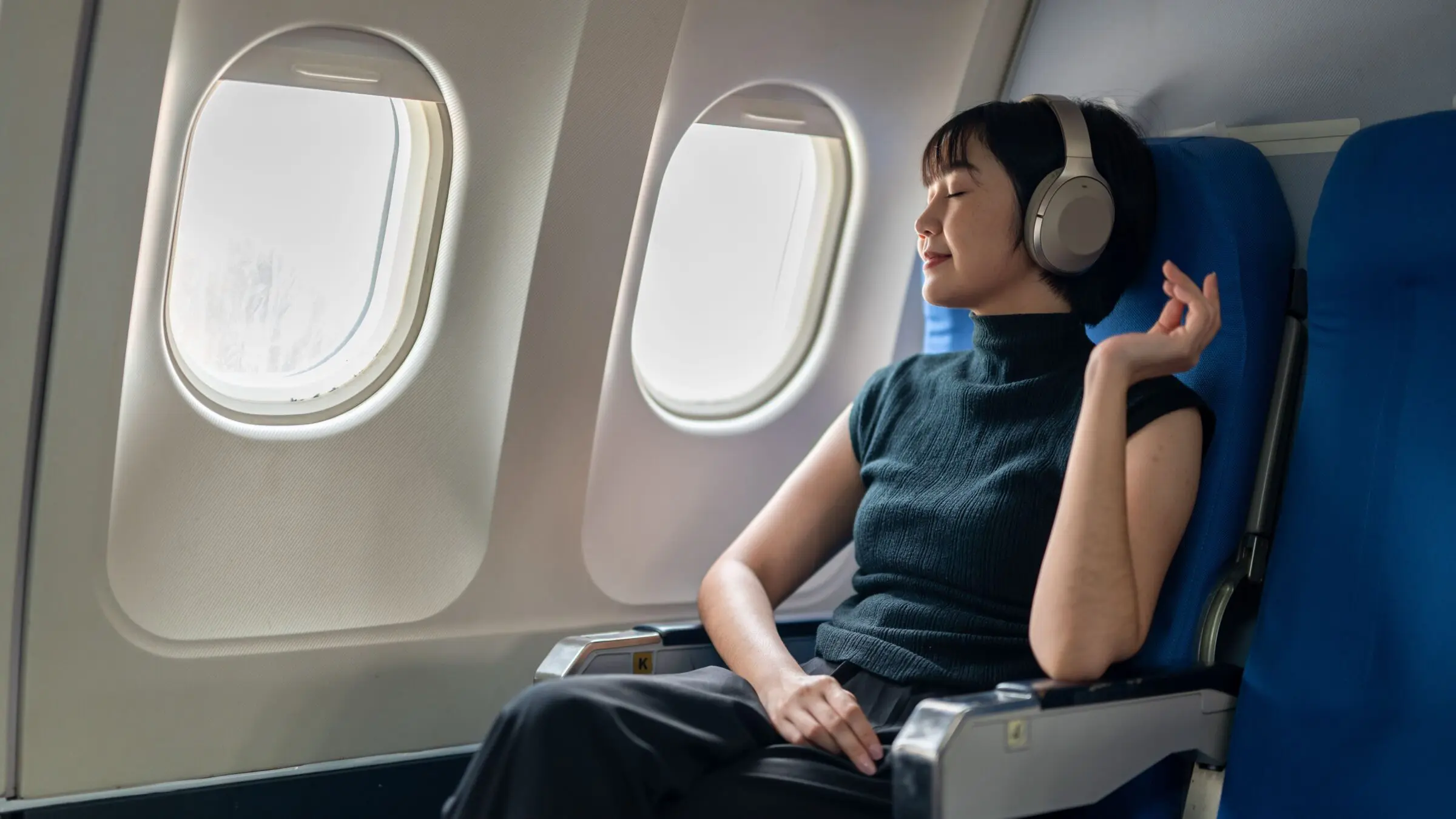 A passenger enjoying music with headphones while sitting in an airplane seat.