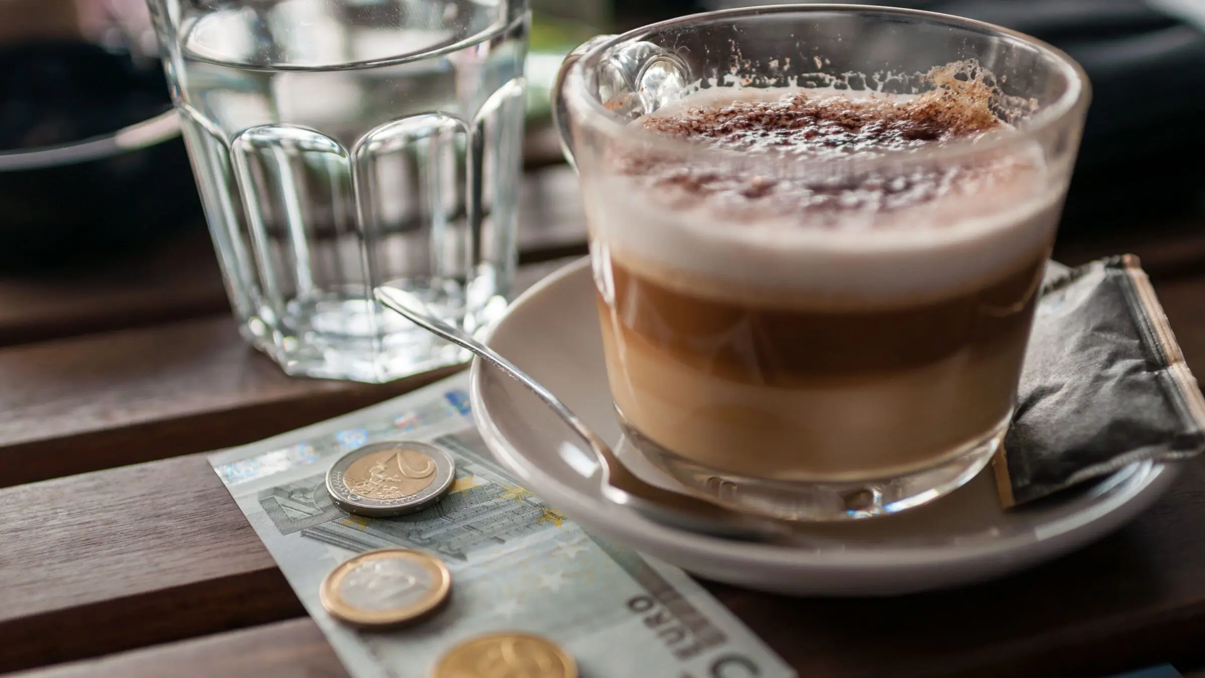 A cup of coffee with a 5 Euro banknote and some coins next to it.