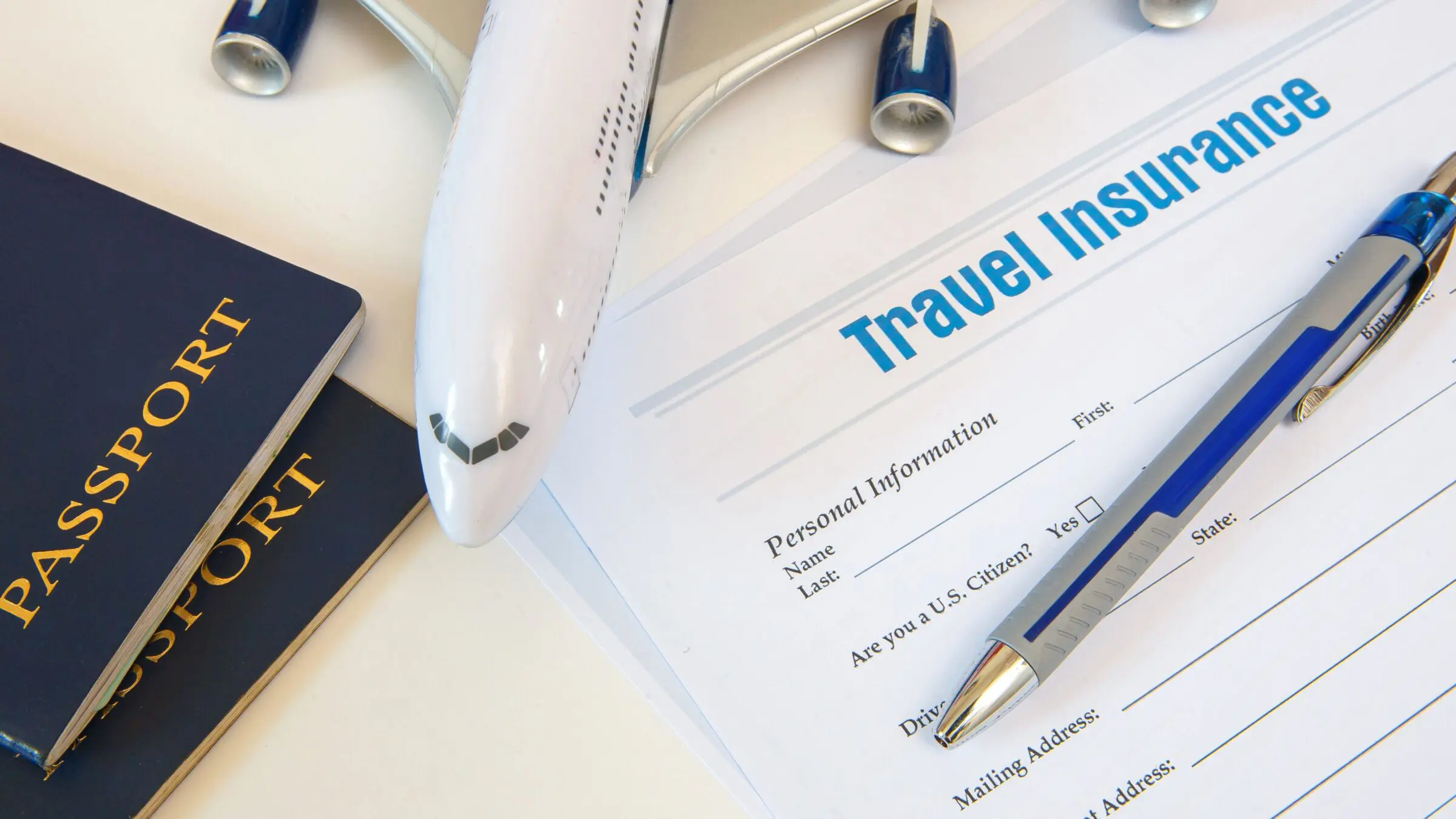 A travel insurance application form, two passports, a pen and a toy airplane.