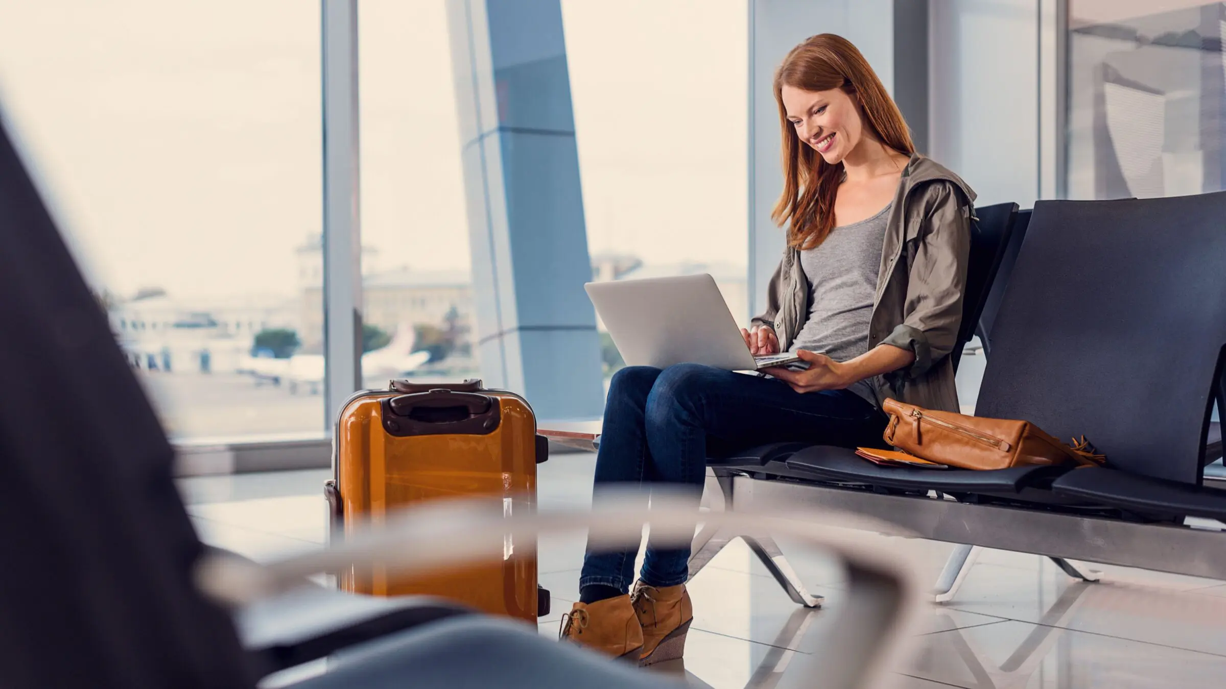 A photo of a smiling young woman holding a laptop while waiting for departure at the airport.