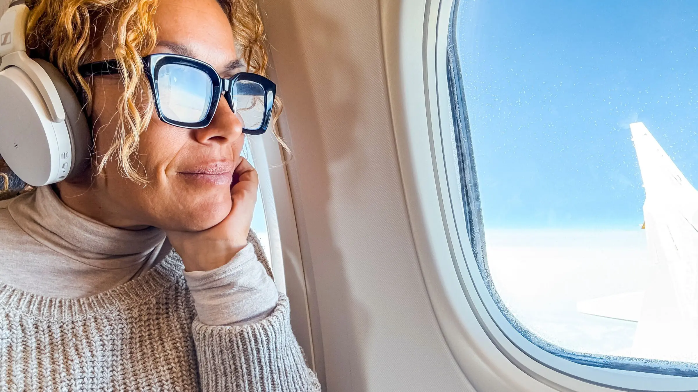A middle-aged woman listens to music and relaxes while sitting in a comfortable airplane seat.