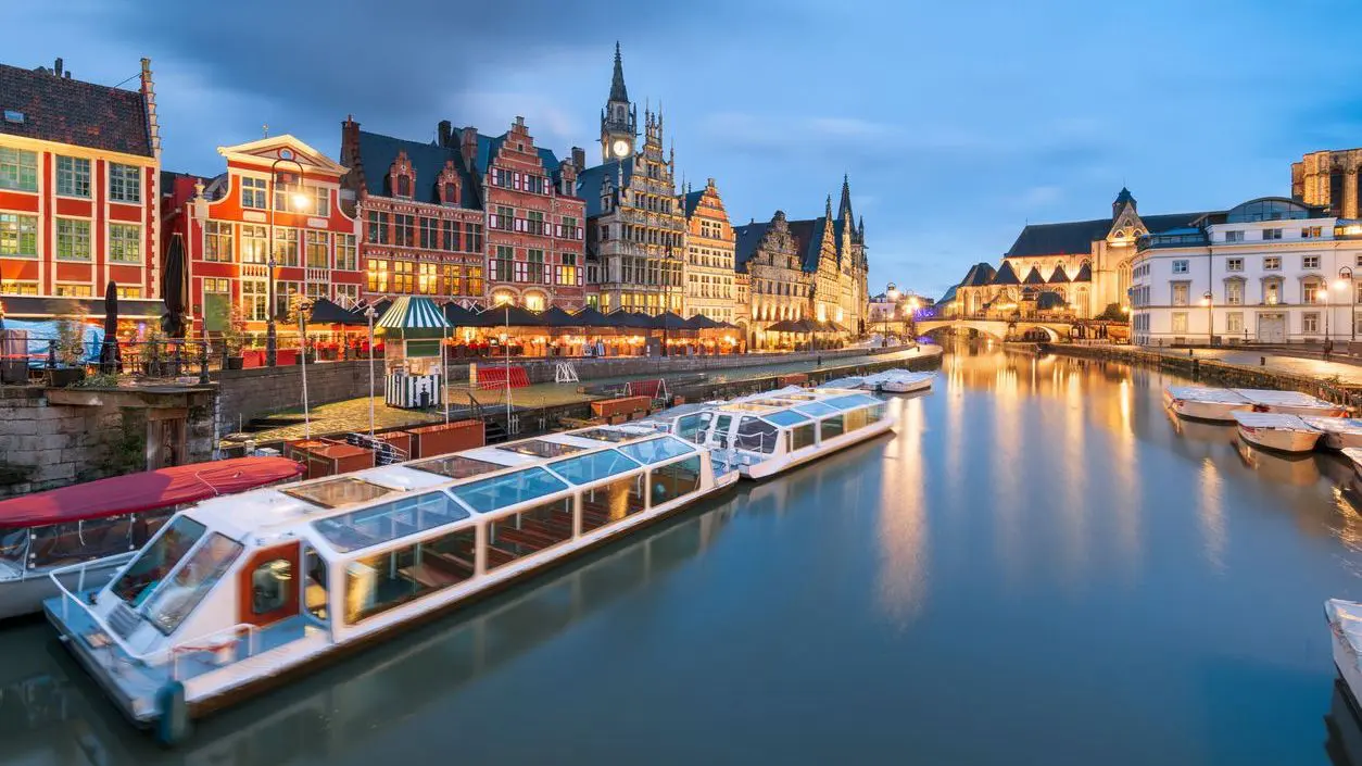 Ghent Old Town cityscape from the Graslei area with river cruise boats at twilight.
