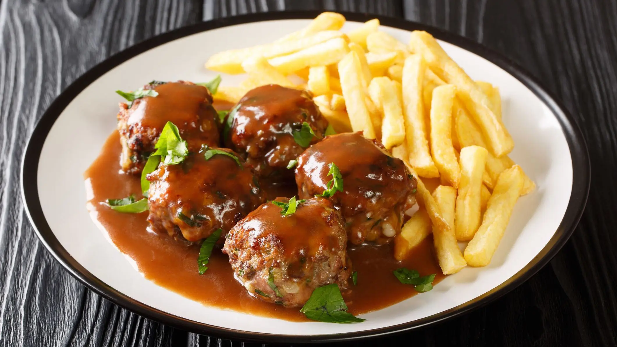 A white dish filled with meatballs and French fries.