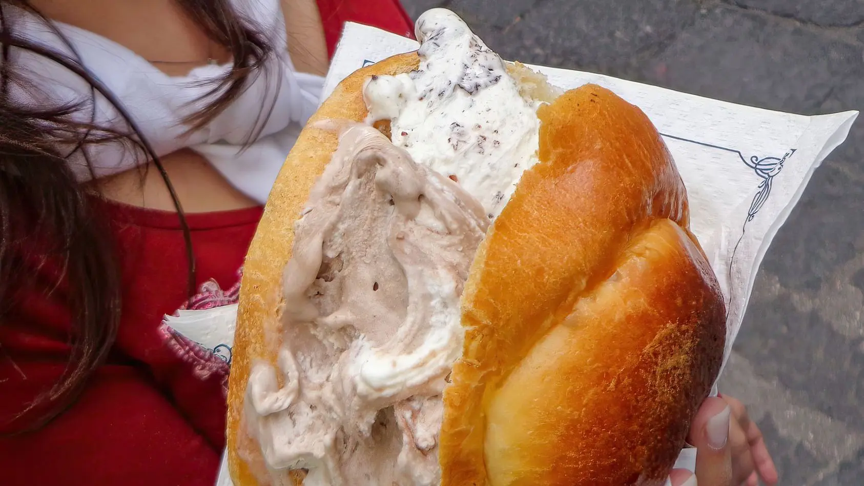 A woman is enjoying a refreshing brioche con gelato, a typical Sicilian dessert, on a sunny day.