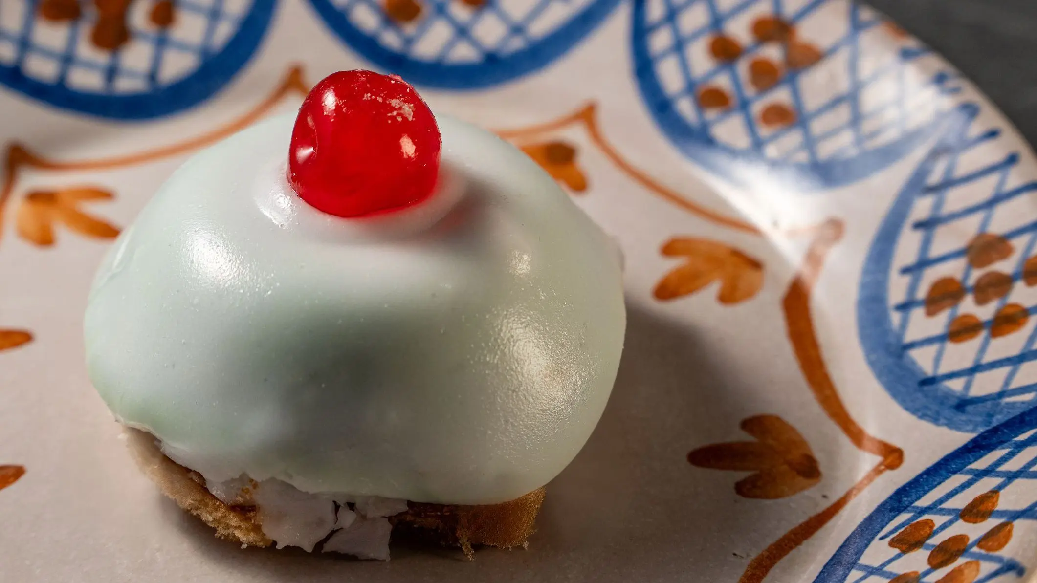 A close-up of a traditional Sicilian mini cassata cake decorated with ricotta, candied fruits, and a cherry on top, served on a beautifully decorated plate.
