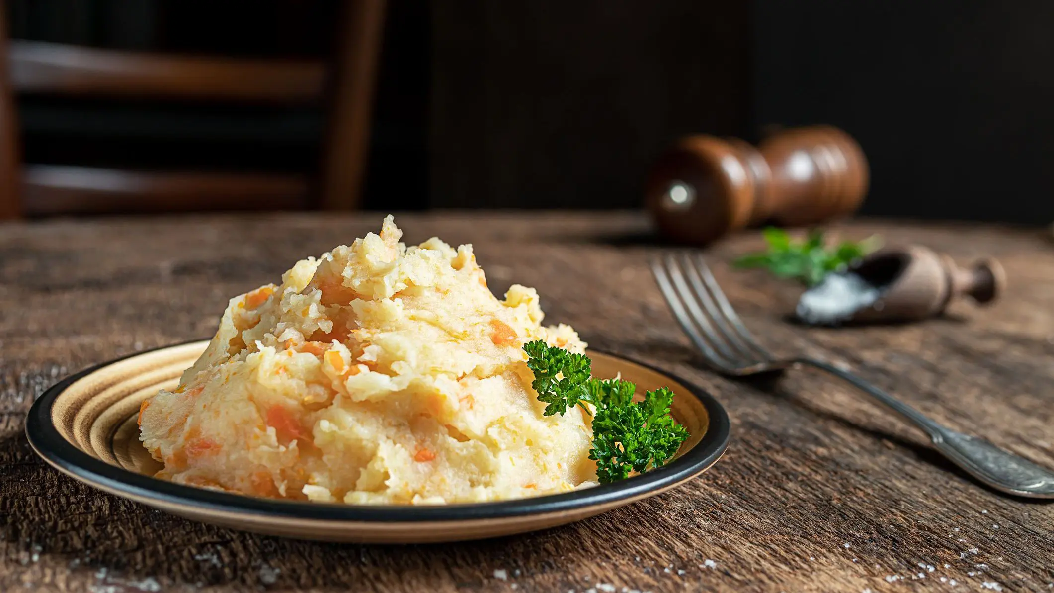 A close-up of mashed parsnips with potatoes and carrots on a dark wooden background.
