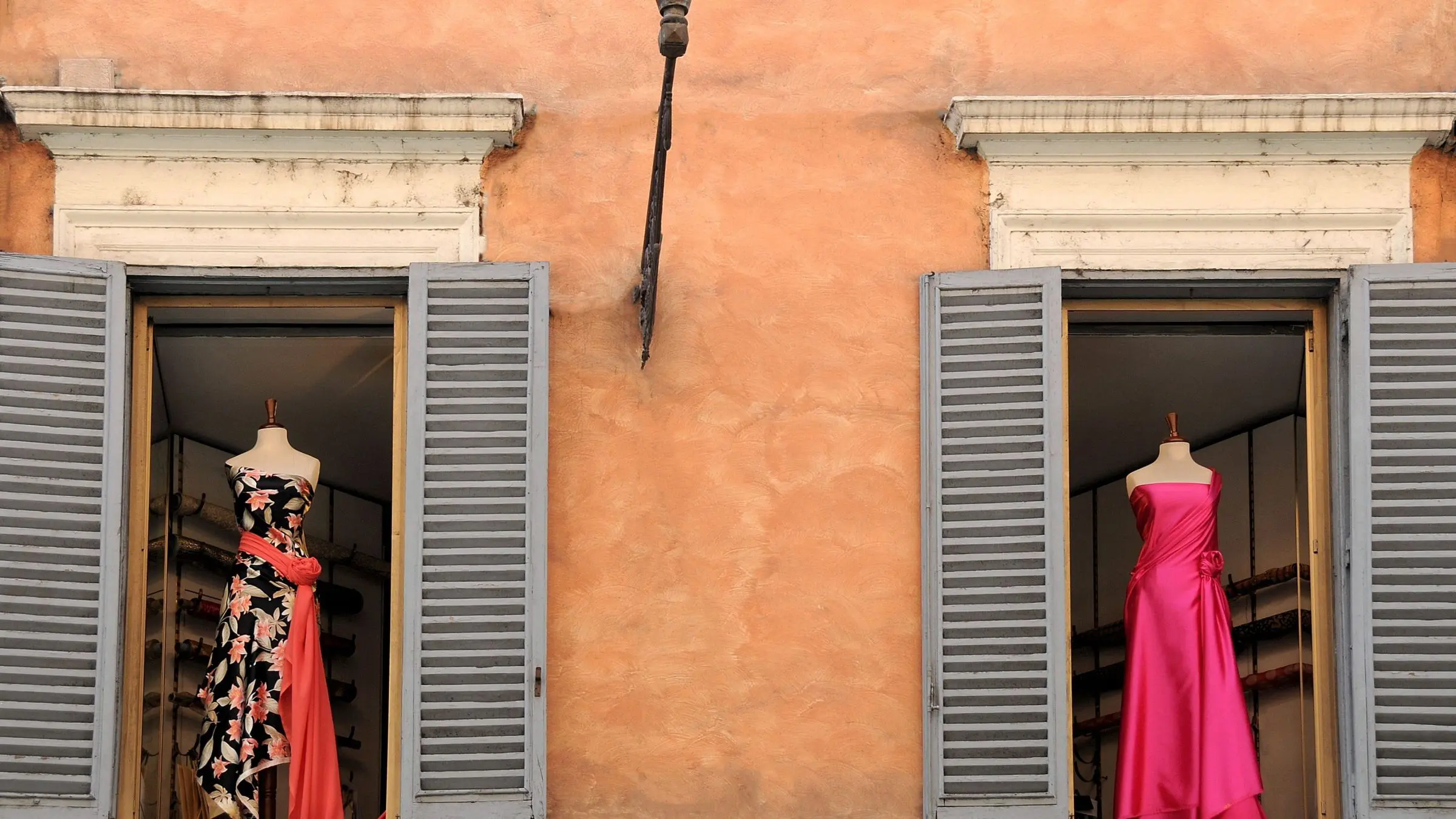 Two dresses displayed on two windows of an old Italian building.