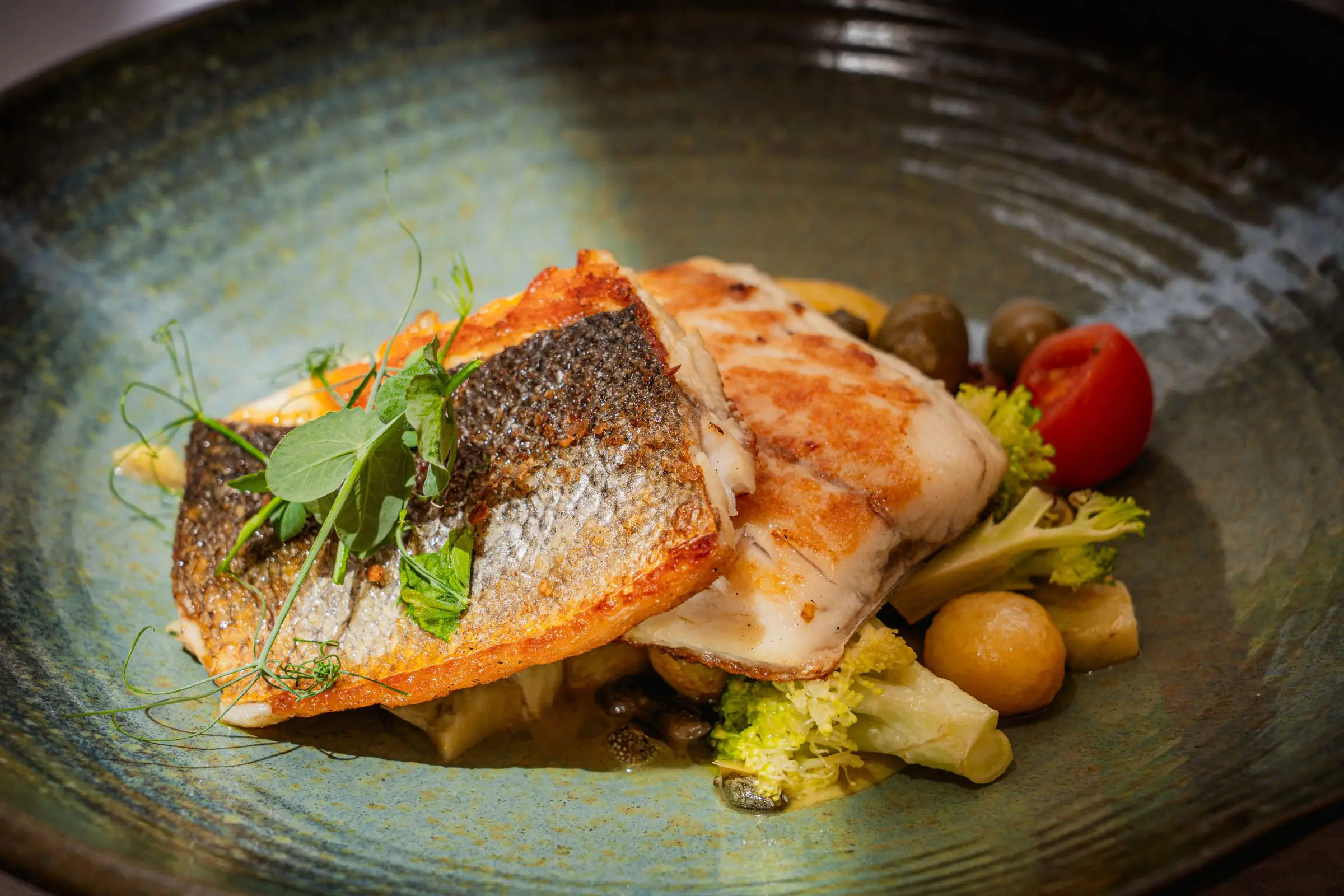 A close-up of a fish-based dish with vegetables on a grey plate.