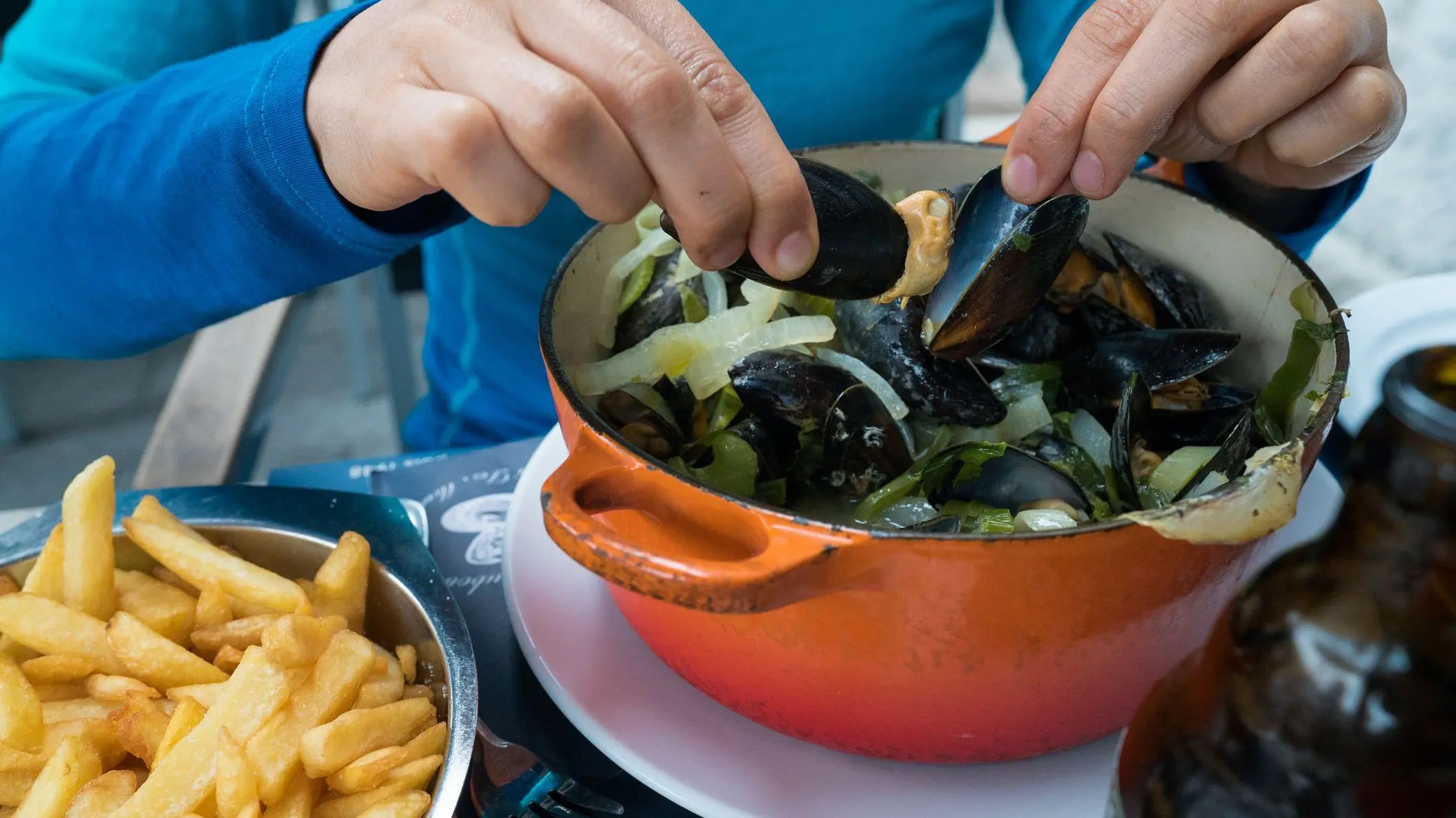 Horizontal view of the hands of a woman eating traditional mussels and French fries, for many, the best Belgian food.