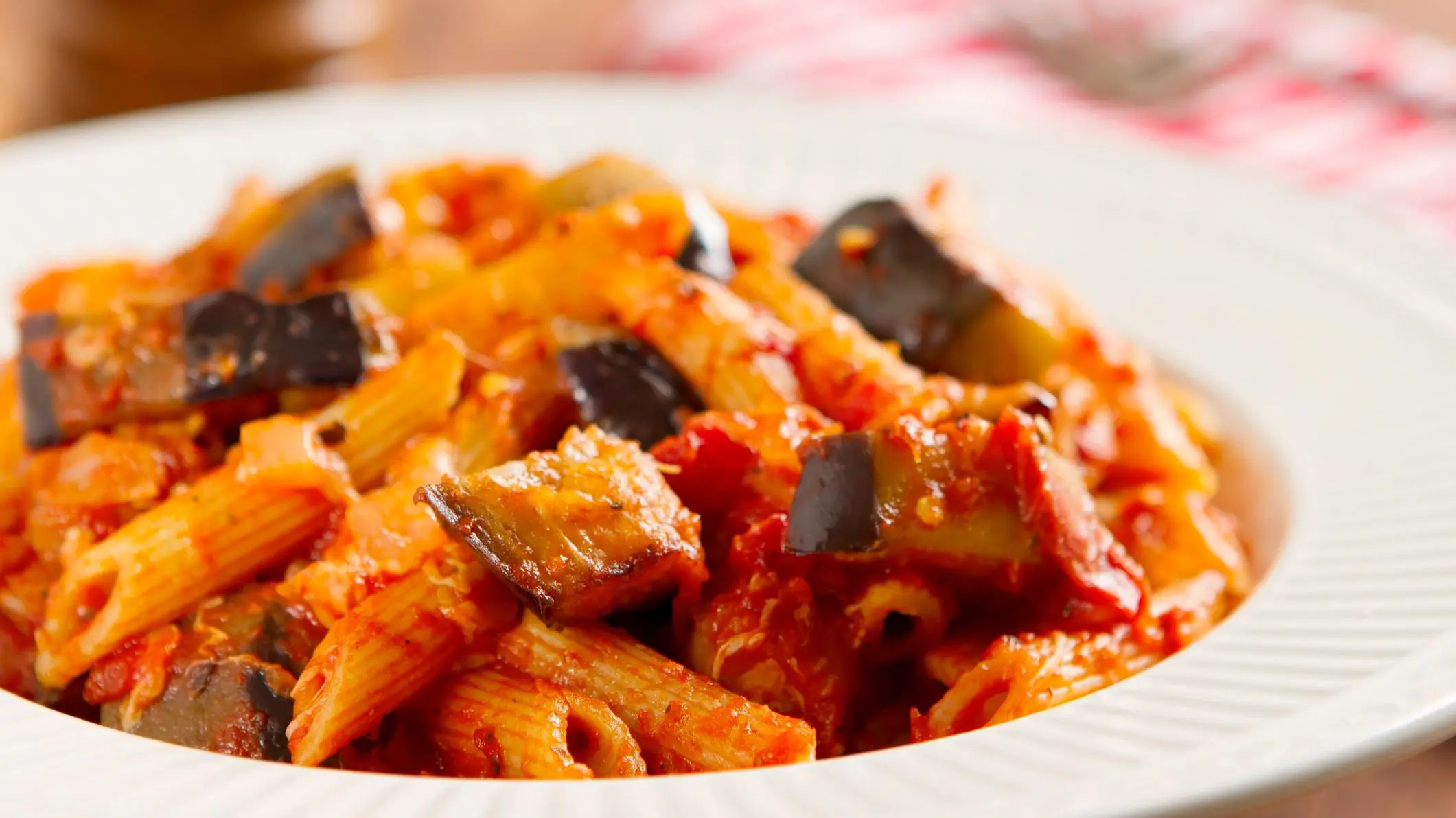 A close-up of the classic Sicilian dish made with rigatoni pasta, fresh eggplant, onion, basil, olive oil, and mozzarella cheese.