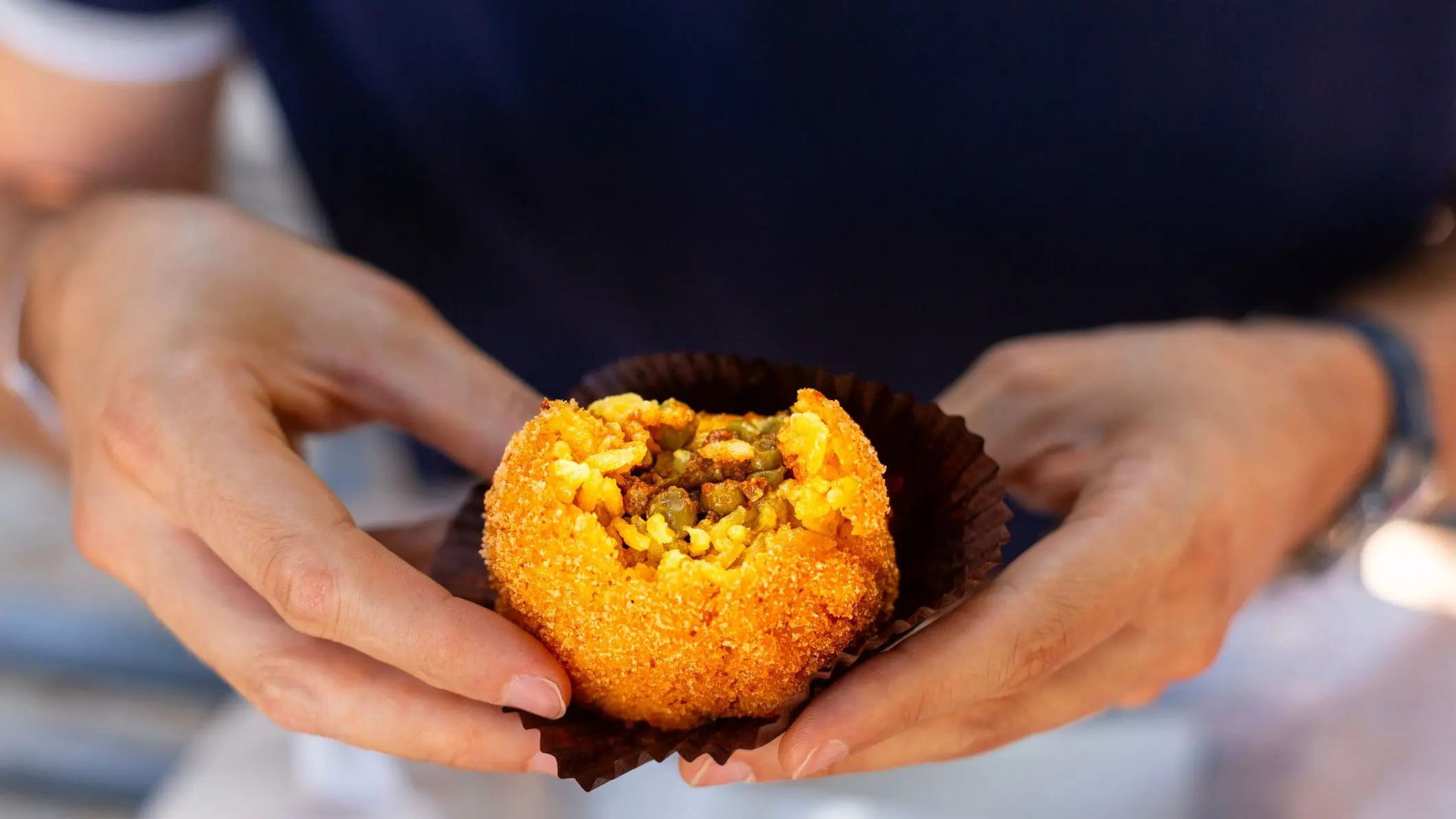 A man is eating arancini, an Italian rice ball al ragu or al sugo, that is stuffed with meat, peas, tomato sauce and spices, coated with breadcrumbs and deep fried.