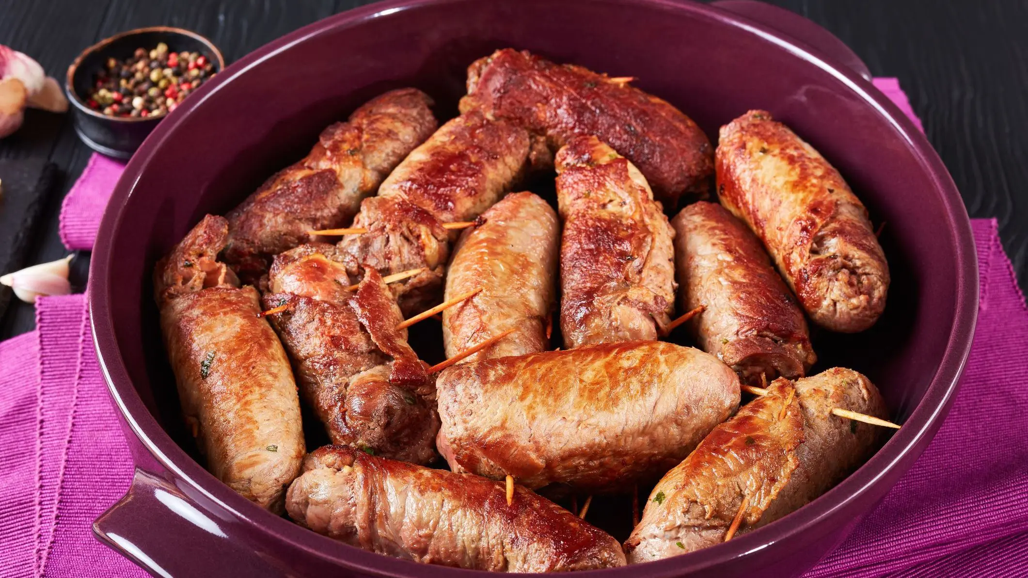 A close-up of fried Italian Braciole: beef steak rolls stuffed with sliced prosciutto, grated parmesan cheese and parsley, pinned with toothpicks.