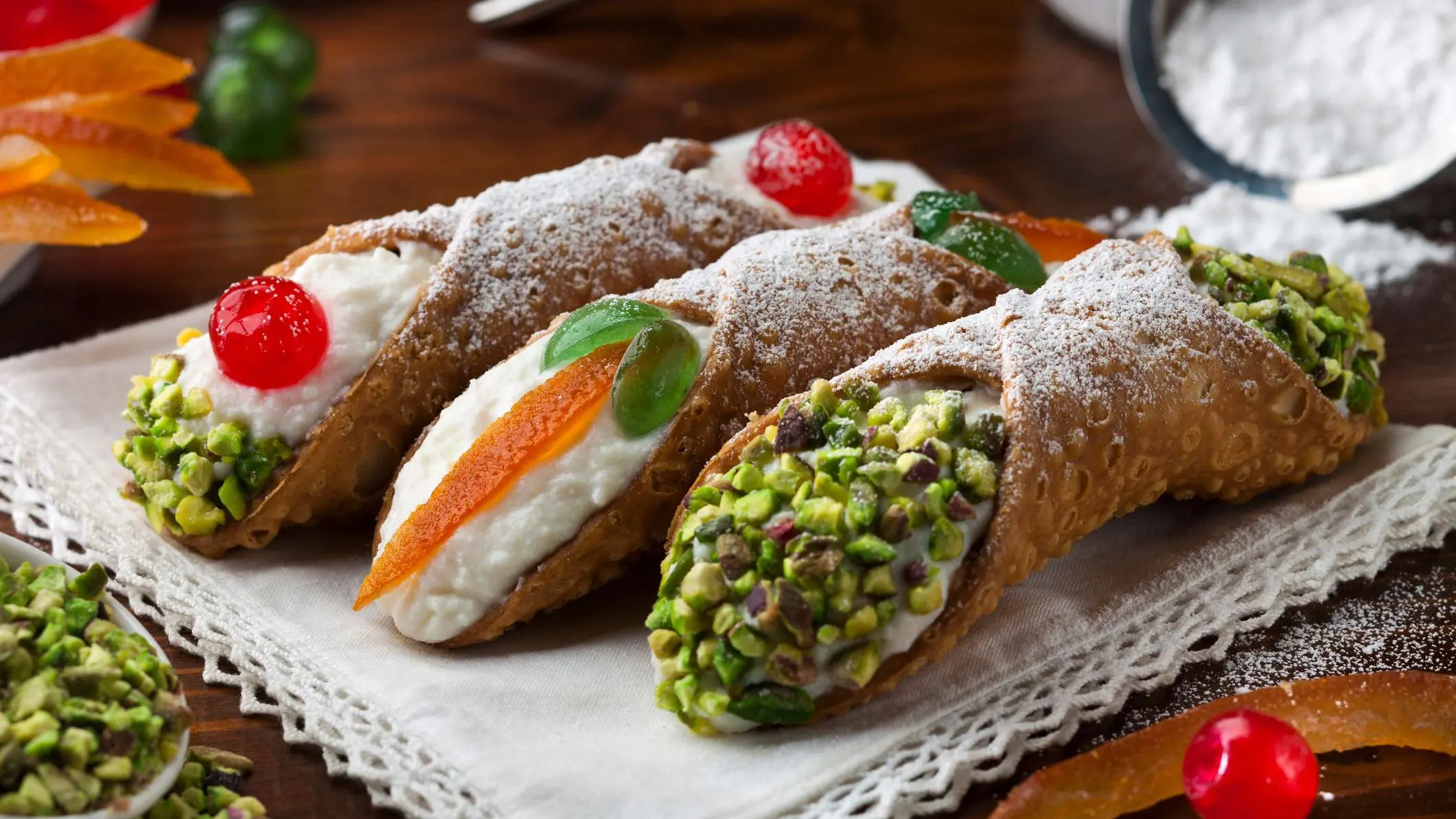 Three Sicilian cannoli with different toppings, such as cherries, pistachios, and candied orange slices.