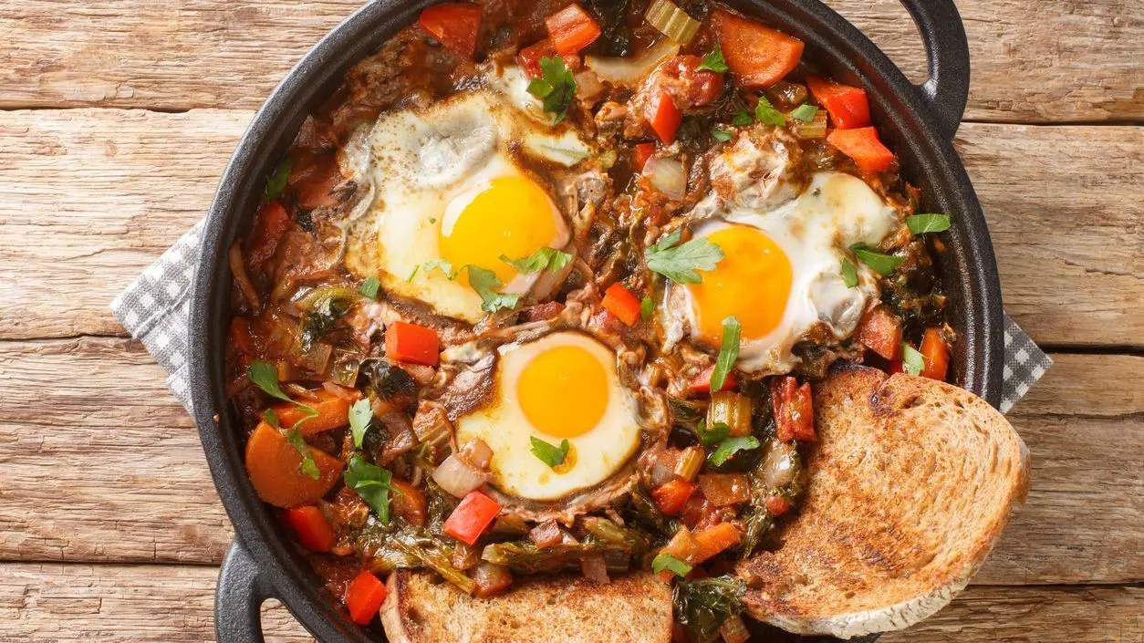 A clay pot with a soup topped with three eggs and two slices of toasted bread.