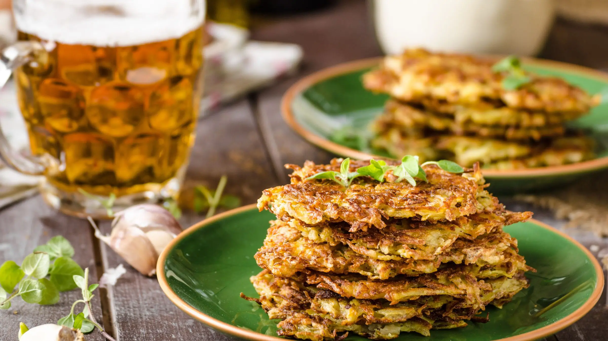 A stack of potato pancakes on a green plate and a mug of beer.