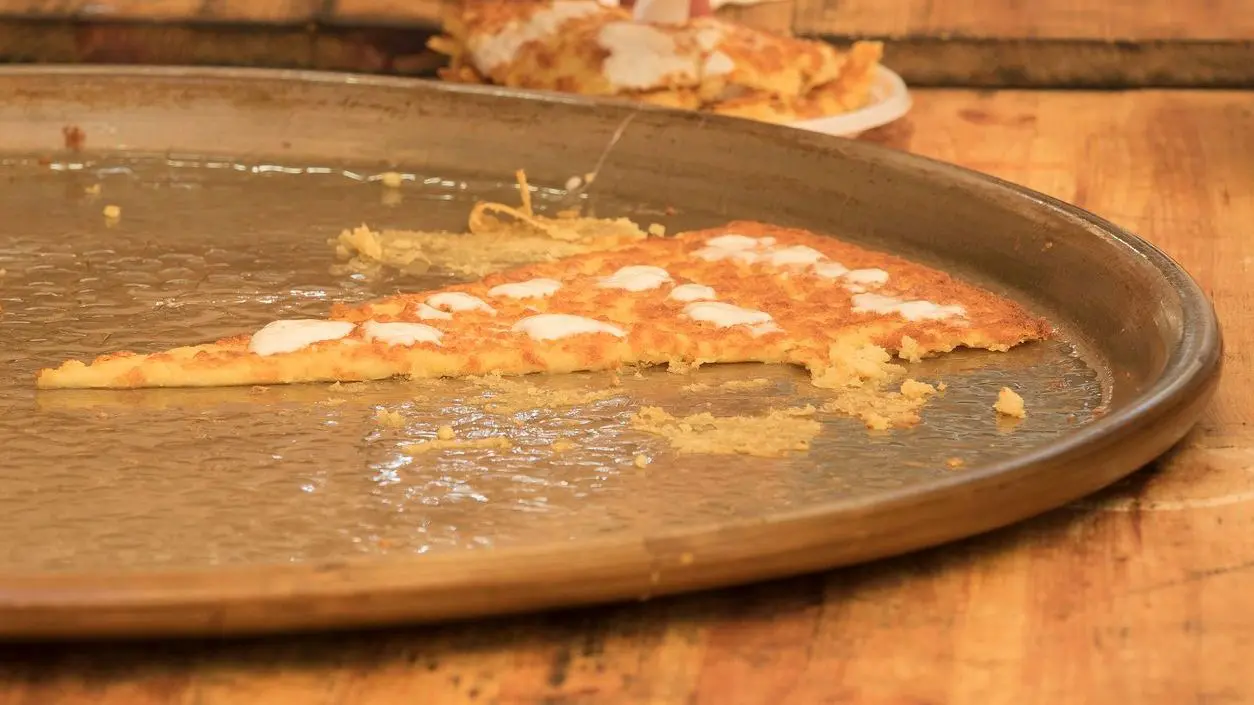 A slice of chickpea farinata or cecina with melted stracchino cheese in a copper pan.