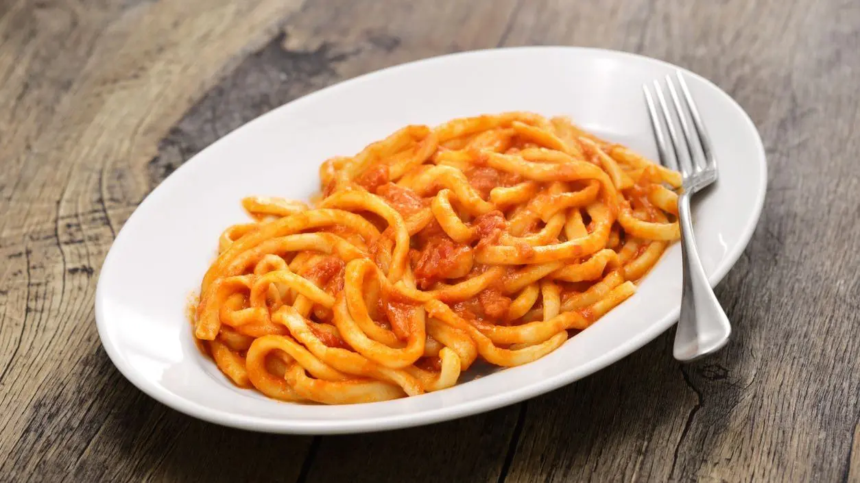 A white plate with thick handmade pasta with garlic tomato sauce.