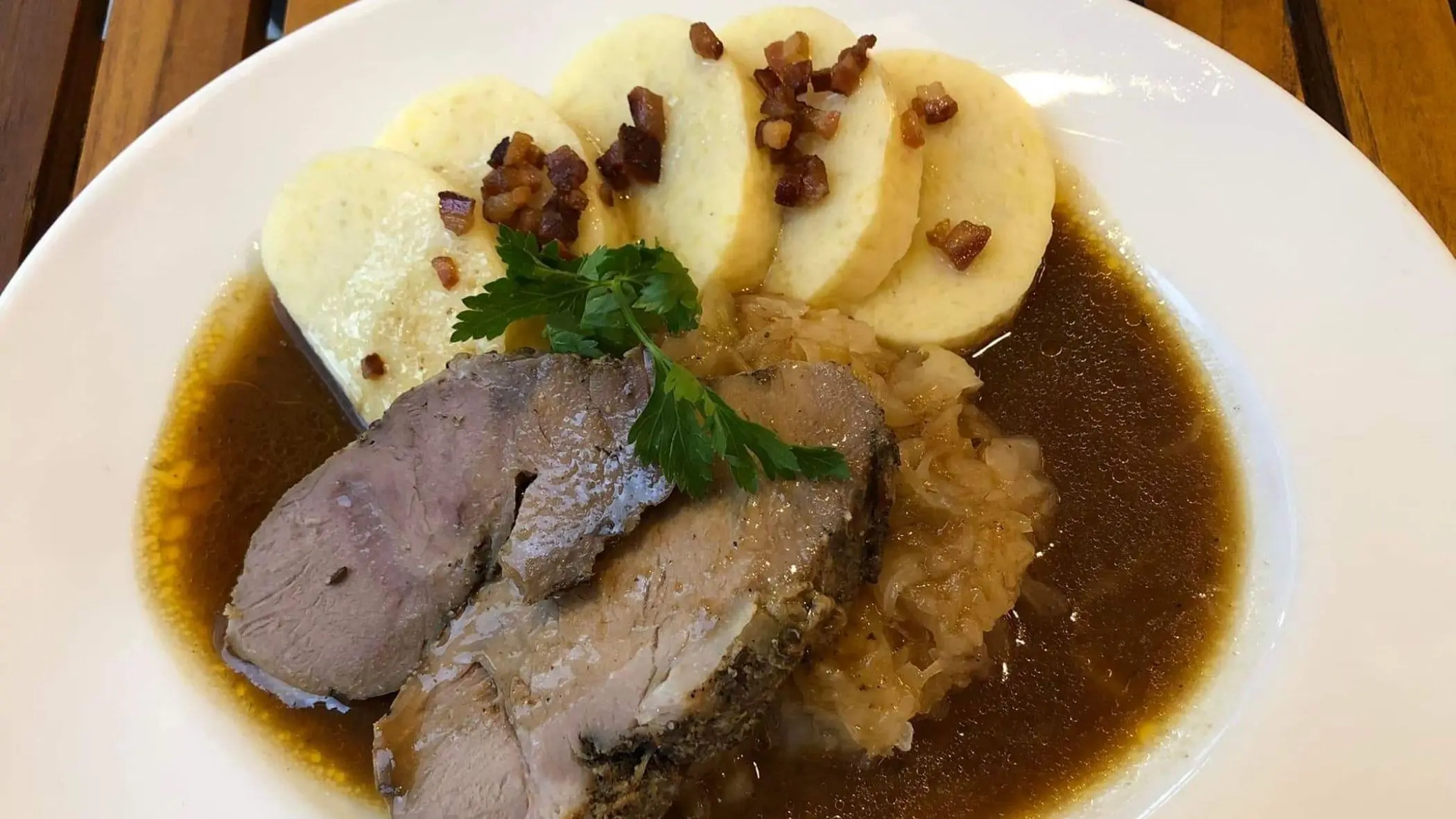 A close-up of a white plate with pieces of meat and bread dumplings in a brown sauce.