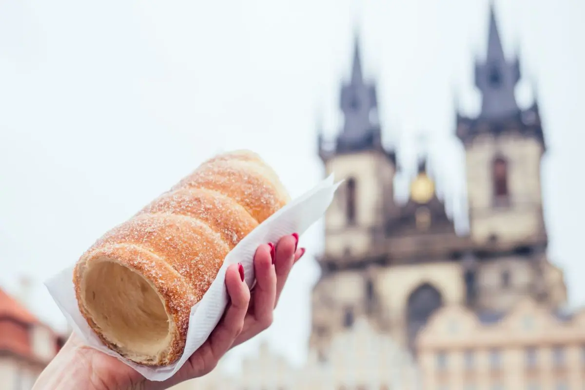 A woman's hand is holding a chimney cake with the Church of Our Lady Before Tyn in the background.