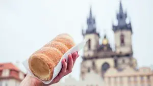 A woman's hand is holding a chimney cake with the Church of Our Lady Before Tyn in the background.