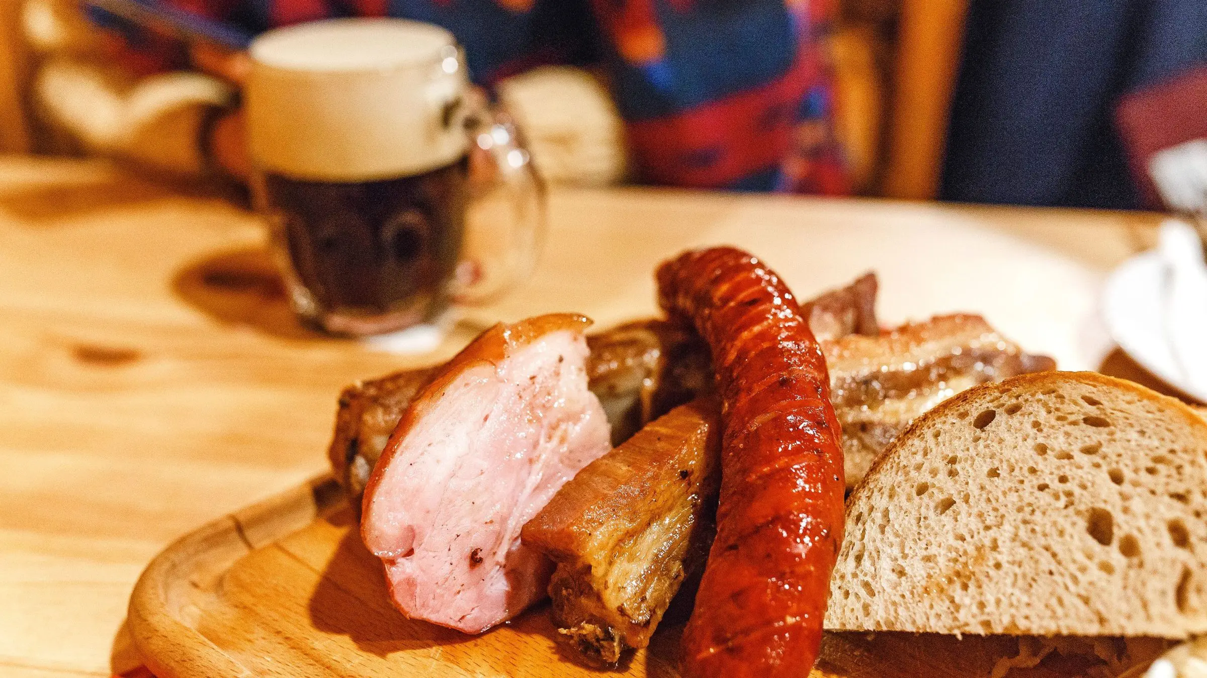A wooden tray with various types of meat and bread and a mug of beer in the background.