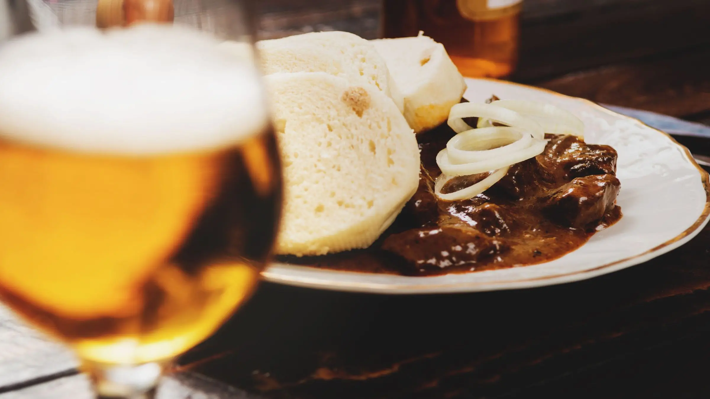 A glass of beer in the foreground and a dish of Czech goulash with bread dumplings, for many the best food in the Czech Republic, in the background.