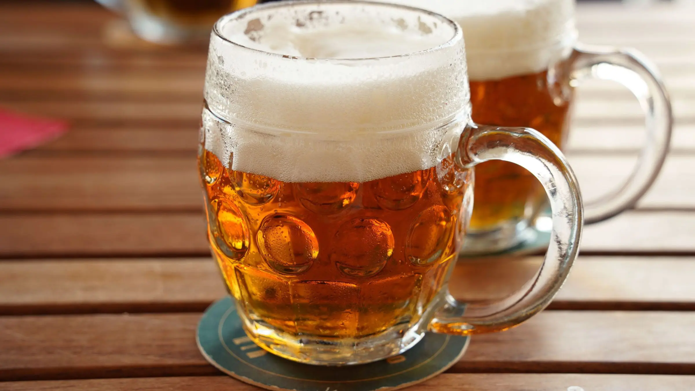Two mugs of beer on a wooden surface.