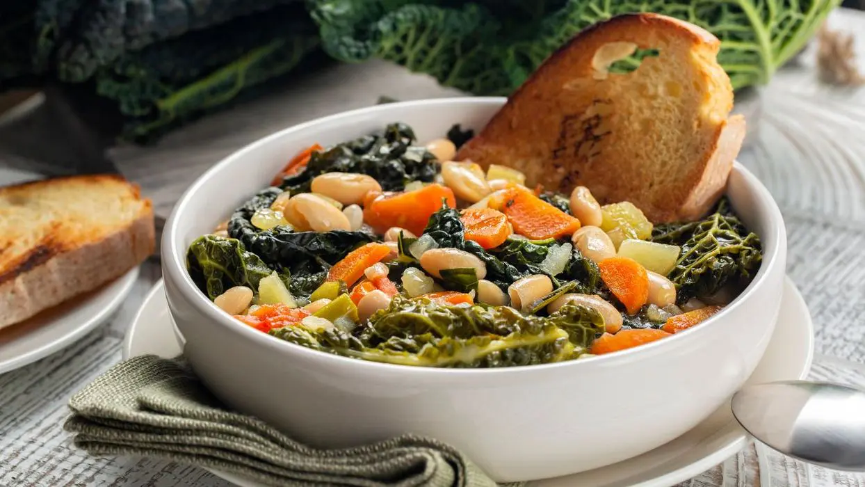 A close-up of a Tuscan vegetarian bread soup made with toasted bread and vegetables, cannellini beans, kale, cabbage, carrots, celery, potatoes, and onion. Ribollita is the best food in Tuscany on a cold day.