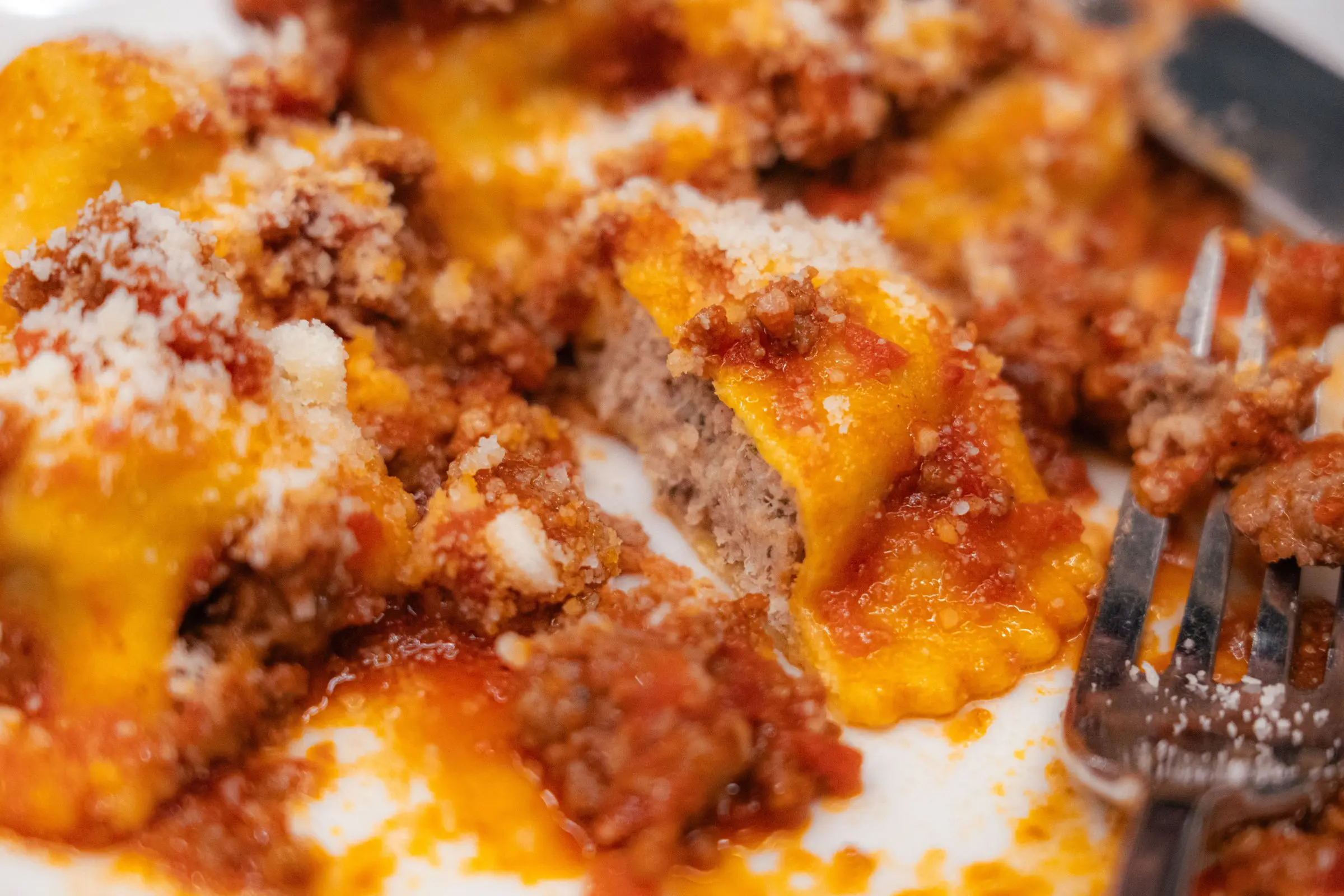 A close-up of pasta stuffed with meat and topped with tomato sauce and parmesan cheese.