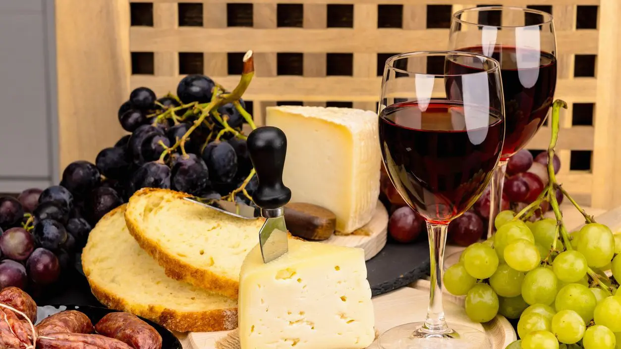 Two glasses of red wine, cheese, bread and grapes.