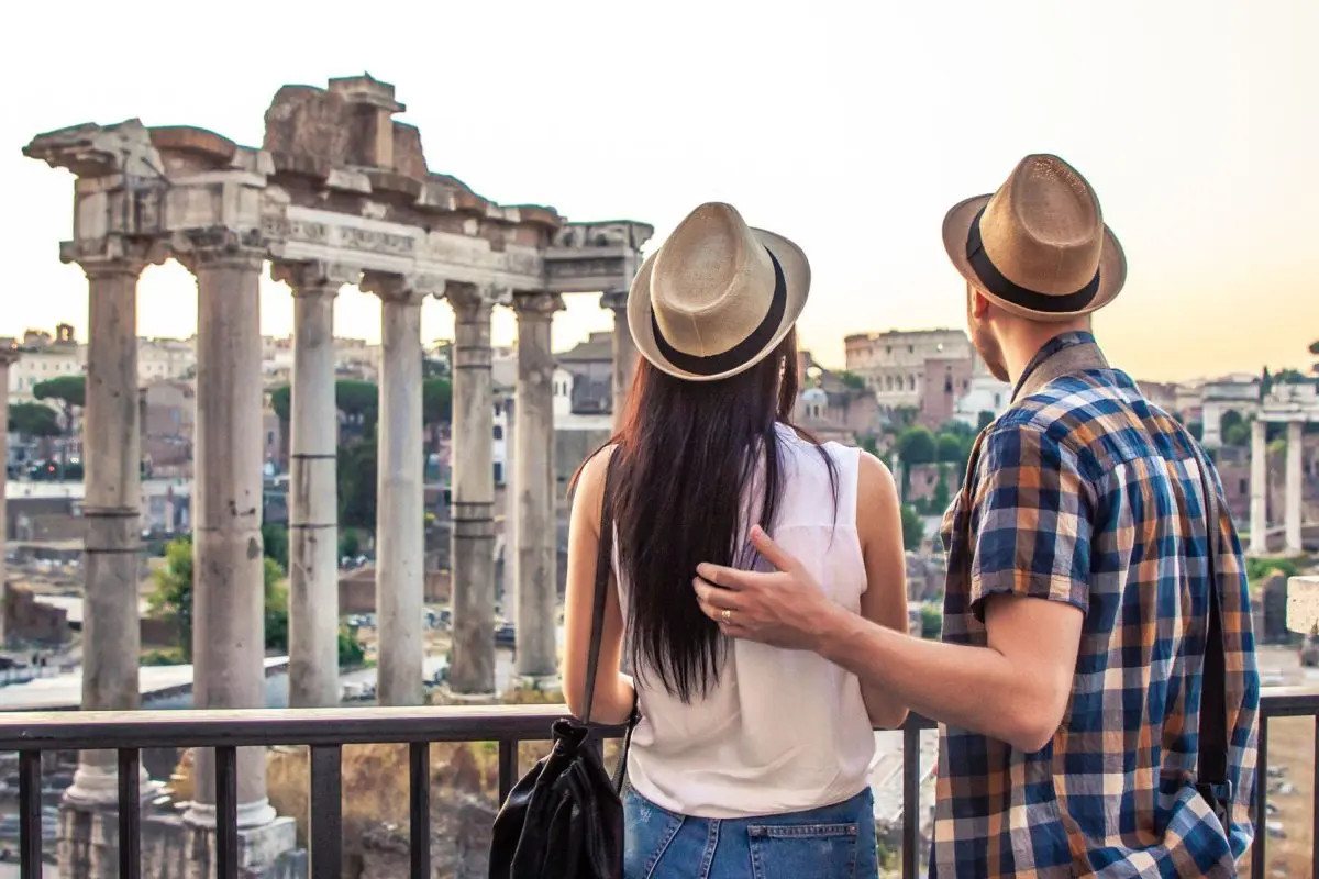 A young couple with their backs turned to the camera are admiring the Roman Forum in Rome.