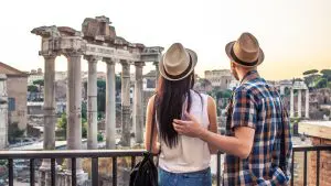 A young couple with their backs turned to the camera are admiring the Roman Forum in Rome.