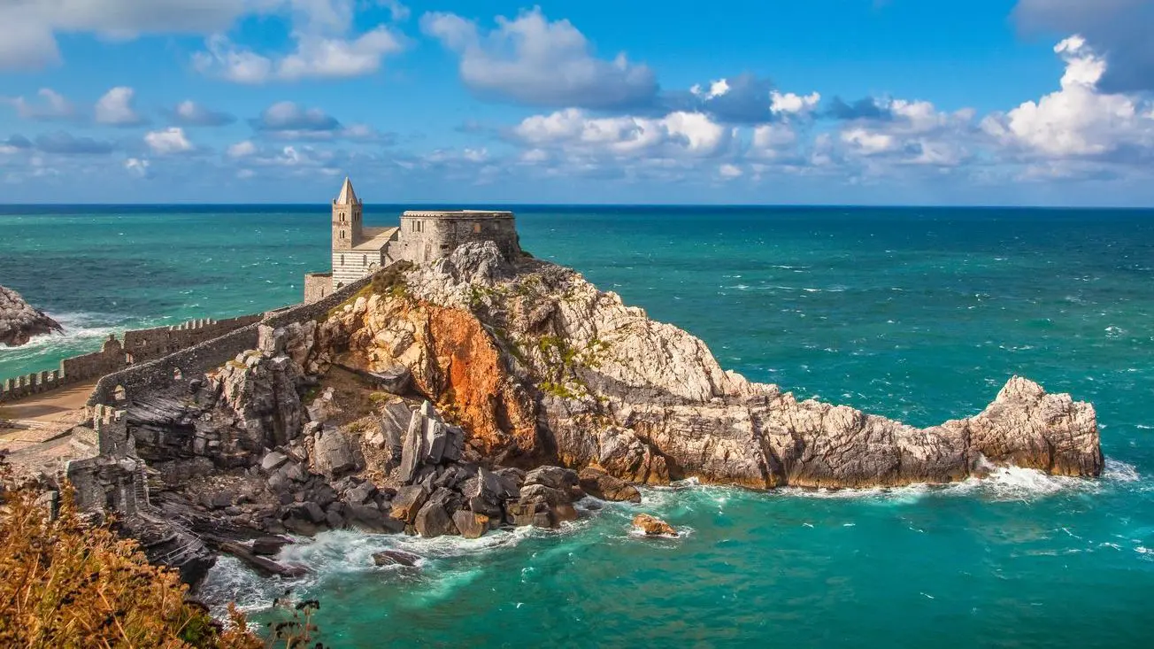 A beautiful view of the famous Gothic Church of St. Peter (Chiesa di San Pietro) perched atop a rocky promontory in the town of Portovenere, one of the best places to visit near Cinque Terre. 