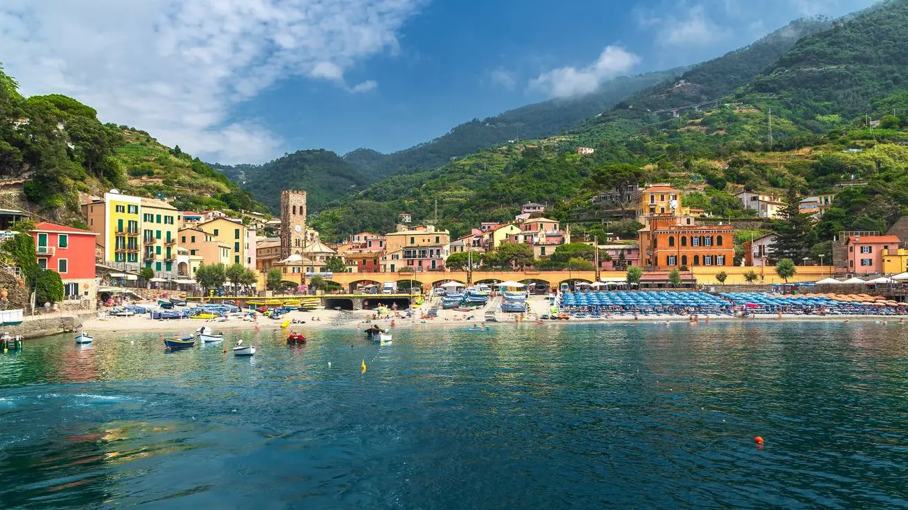 A panoramic view of Monterosso al Mare with its colorful buildings and umbrellas on the beach as seen from the sea. 