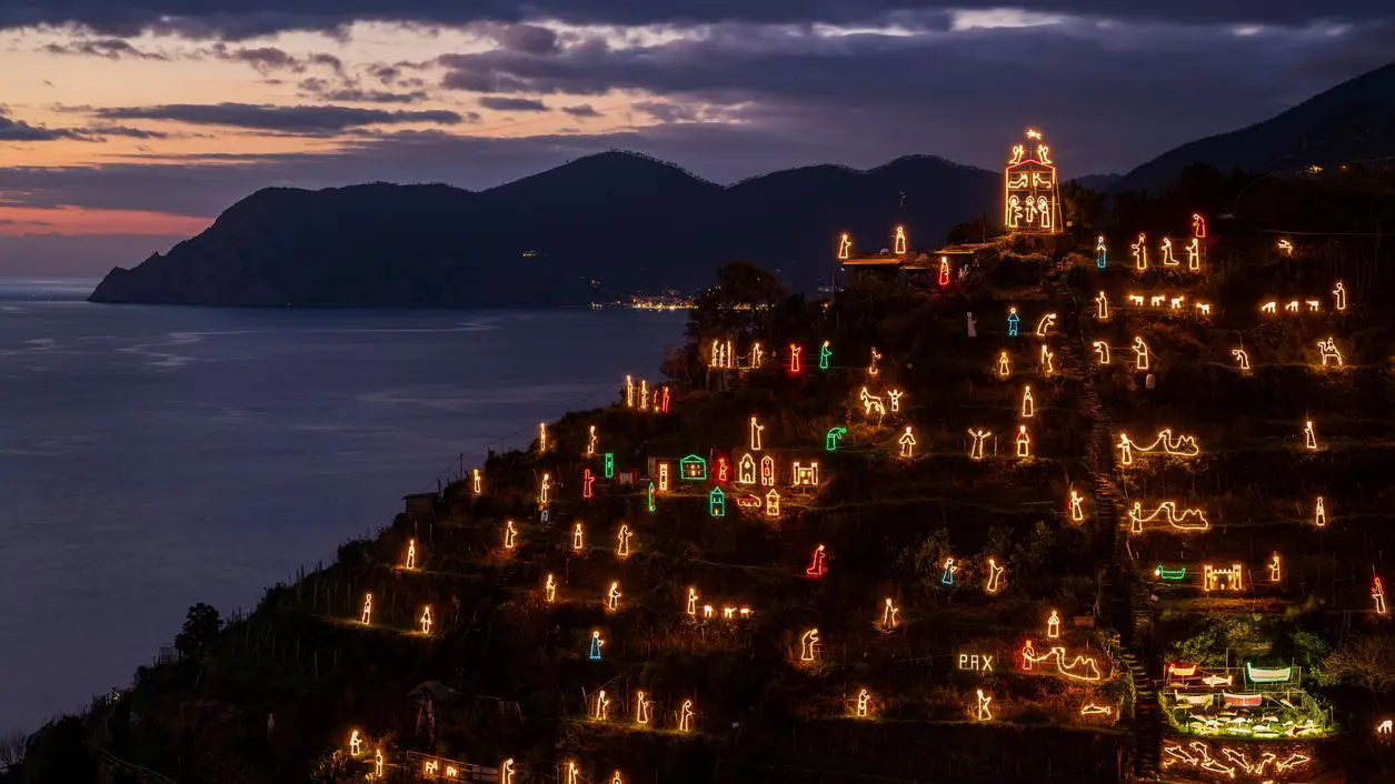 An illuminated Nativity Scene on the top of a hill over the village of Manarola in Cinque Terre at dusk.