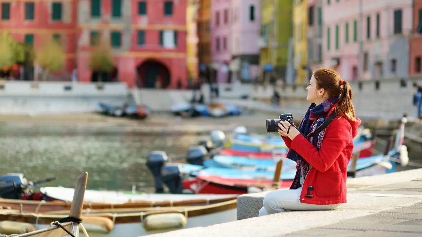 A young woman wearing a red jacket and carrying a camera is enjoying the view of Vernazza, one of the best places to visit in Cinque Terre. 