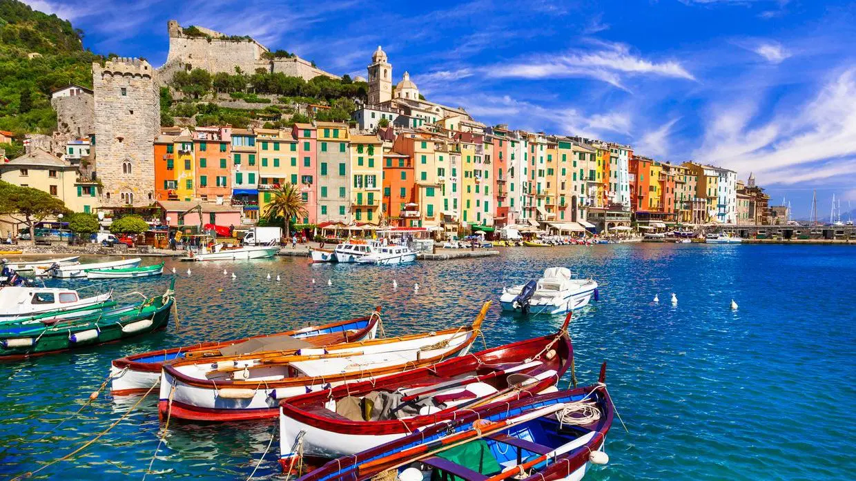 Colorful beachfront buildings in Portovenere and traditional wooden boats on blue waters in the foreground. 