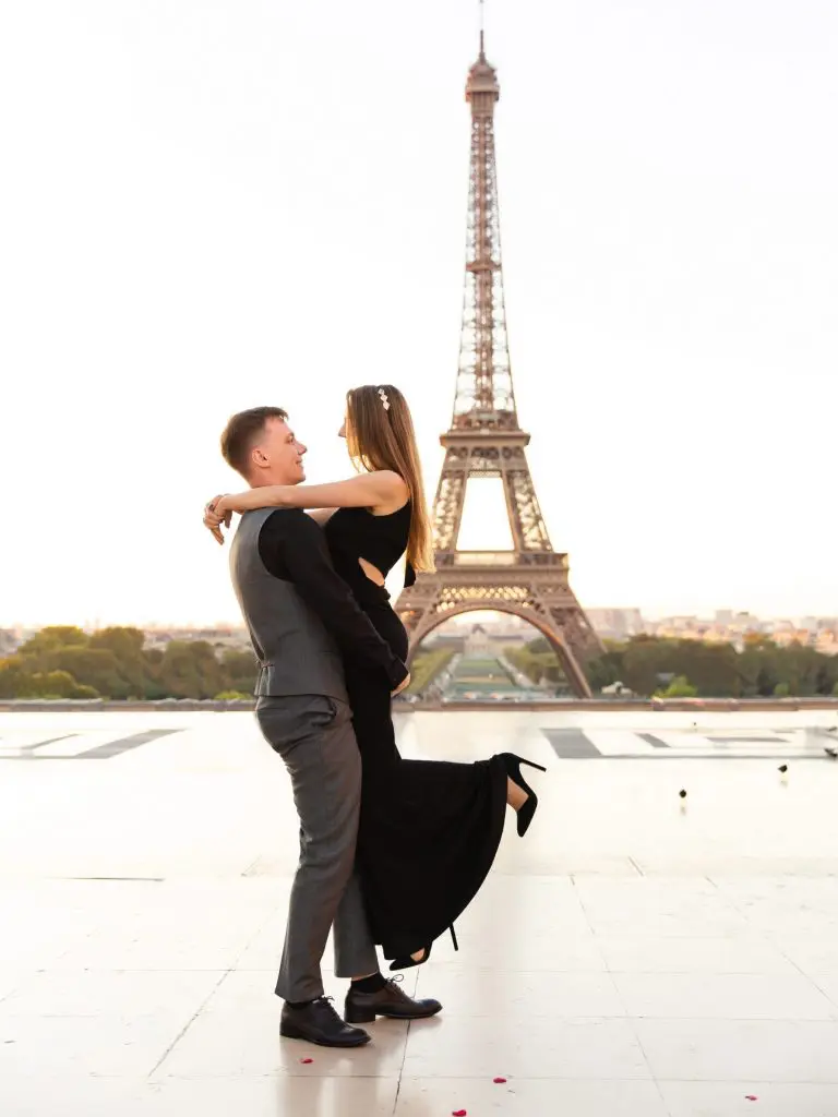 A romantic couple embracing in front of the Eiffel Tower in Paris, France, capturing an elegant European travel moment at sunrise.