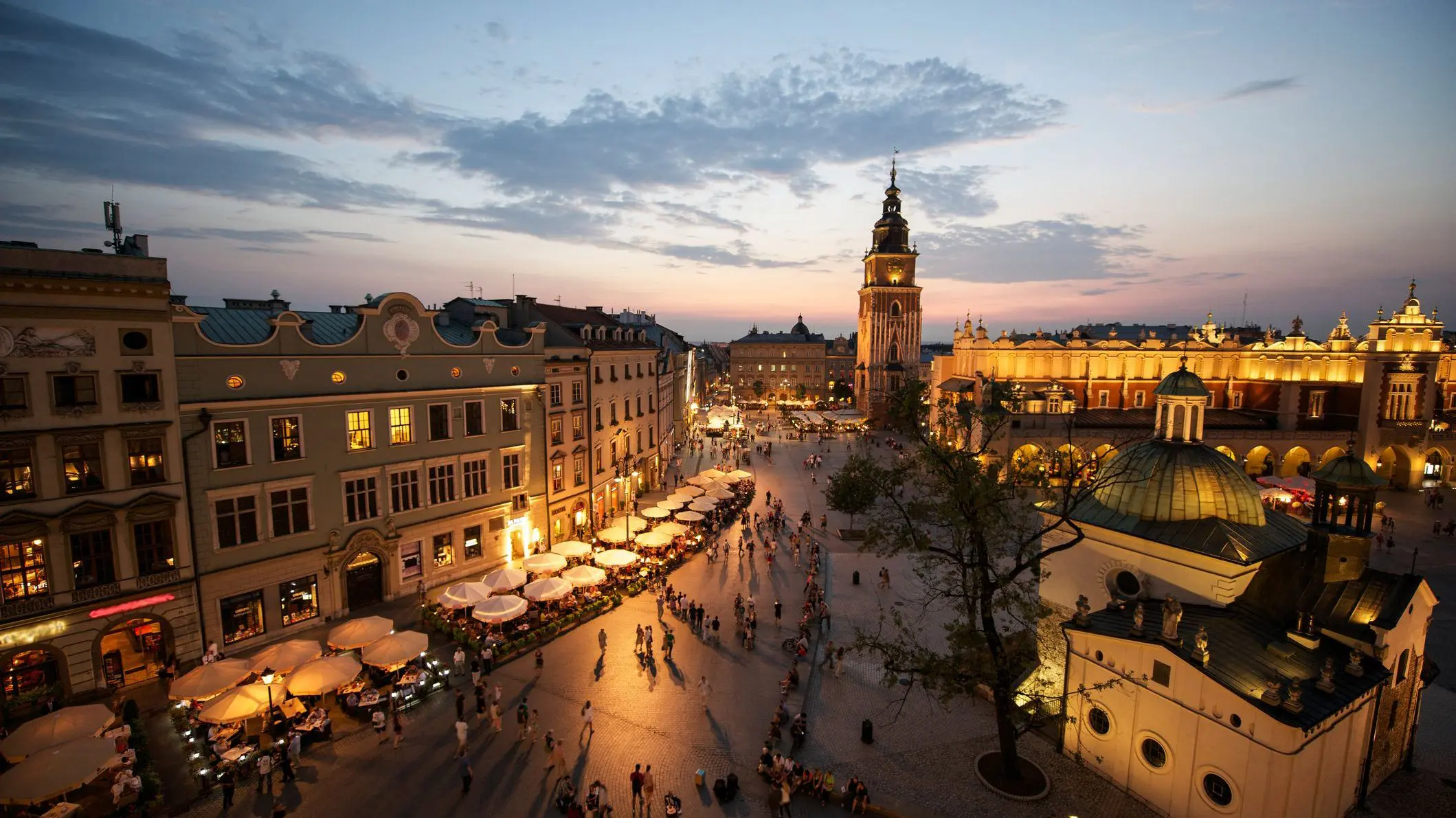 Krakow market square at sunset with night lights on.