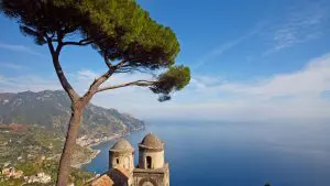 A typical Italian pine tree framing a magnificent view of the Mediterranean coast line from the beautiful gardens of Rufolo in Ravello with a stone church in the foreground.