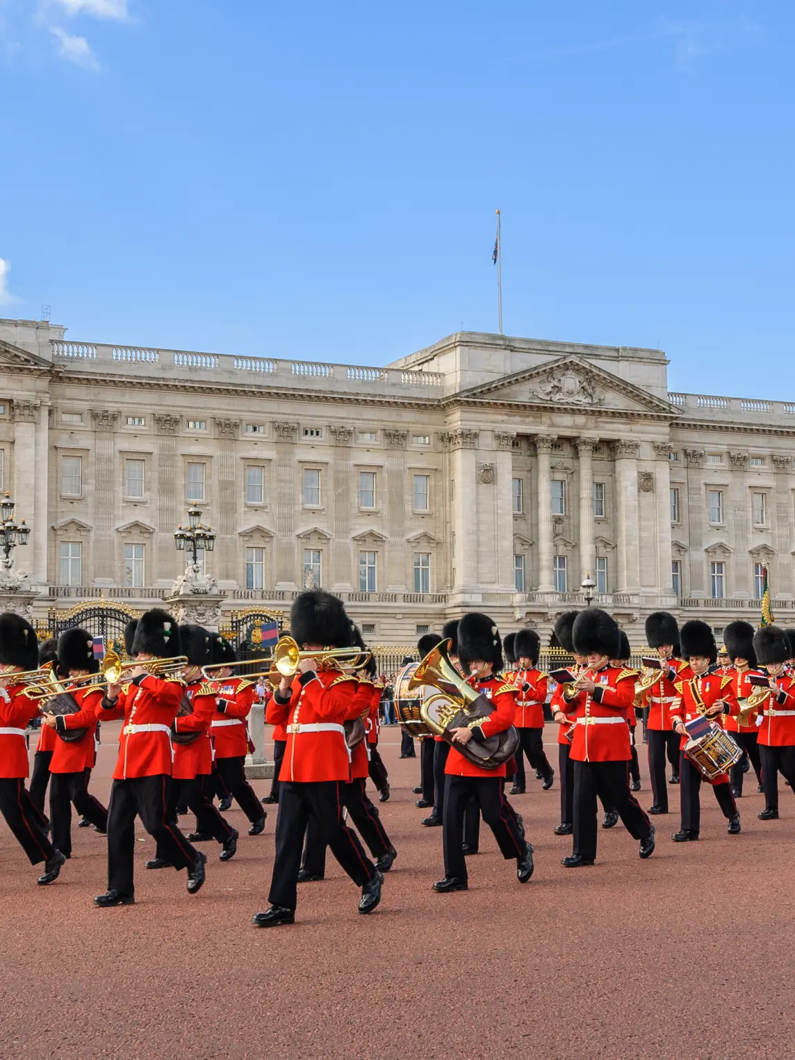 Buckingham Palace featuring its iconic grey stone facade, central balcony, and the Victoria Memorial in the foreground