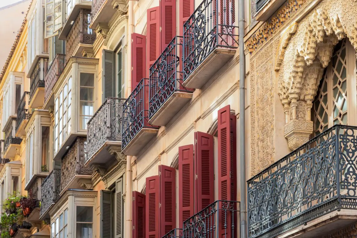 A close-up of elaborate balconies with red shutters in Malaga, Spain.