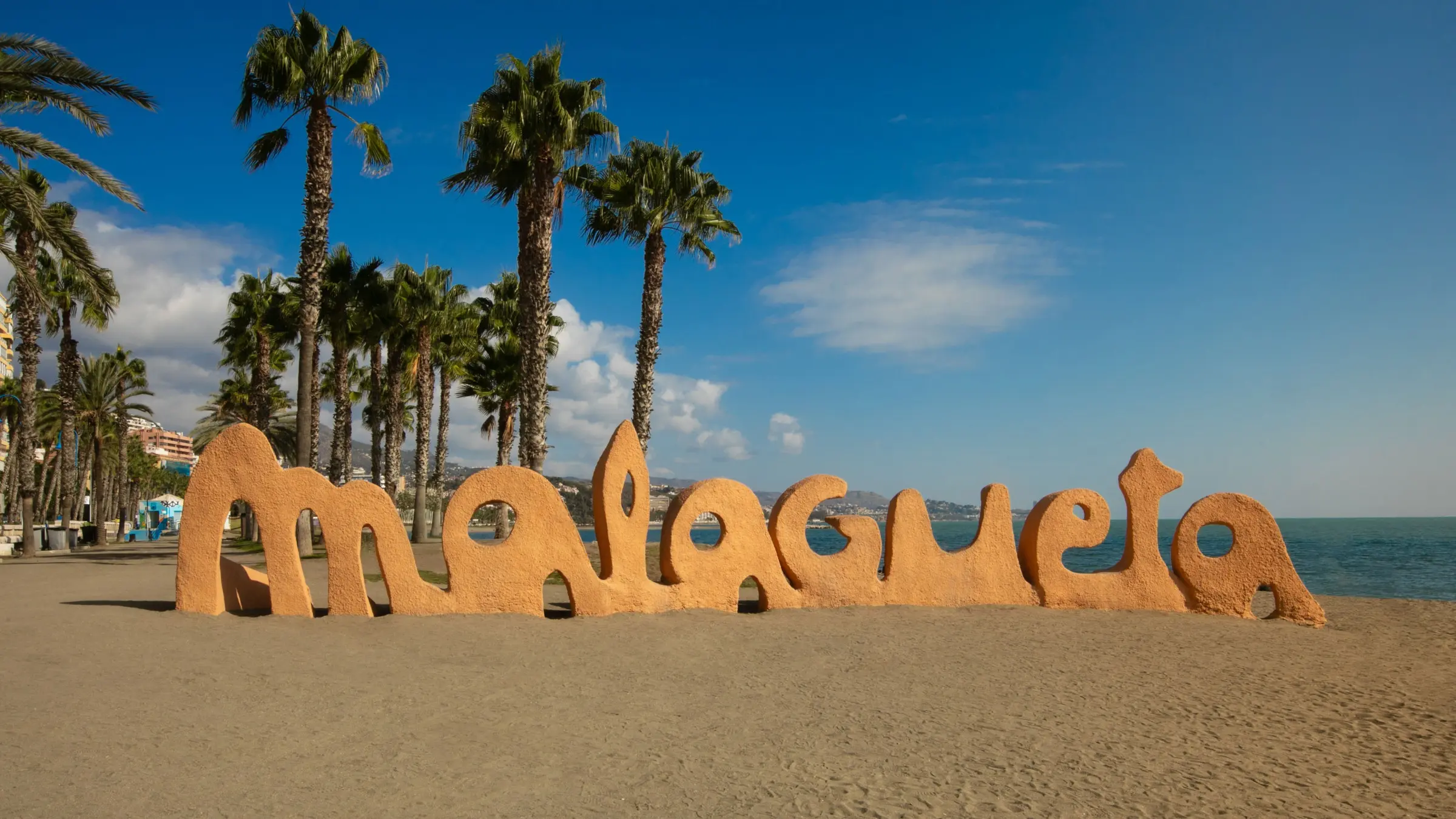 A sign reading Malagueta on the sand by the sea with palm trees in the background. 