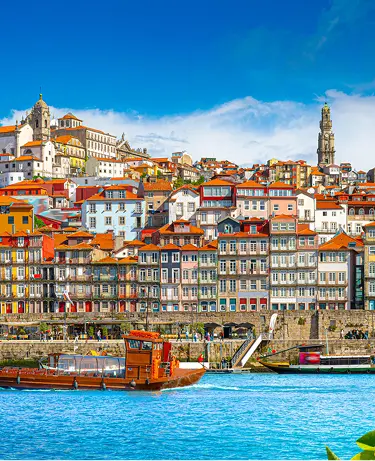 Colorful riverside buildings along the Douro River in Porto, Portugal, with traditional rabelo boats in the foreground