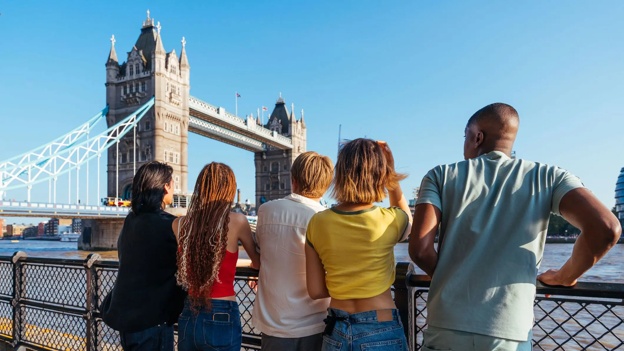 Multiracial group of happy young people looking at the Tower Bridge with their backs turned to the camera.